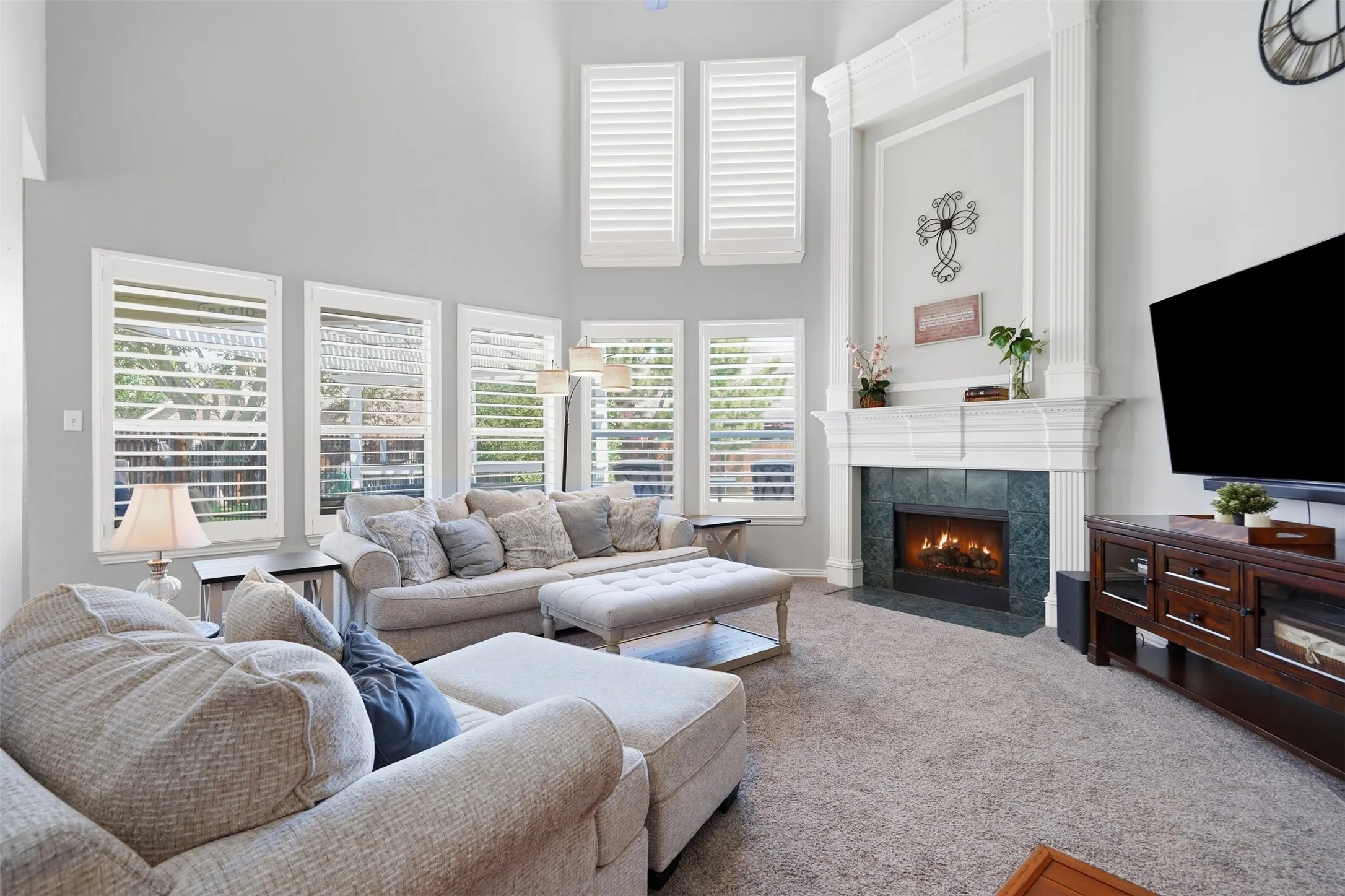 The dramatic two story family room is anchored by an gorgeous fireplace with double mantel, expansive windows, soaring ceilings, and elegant plantation shutters.