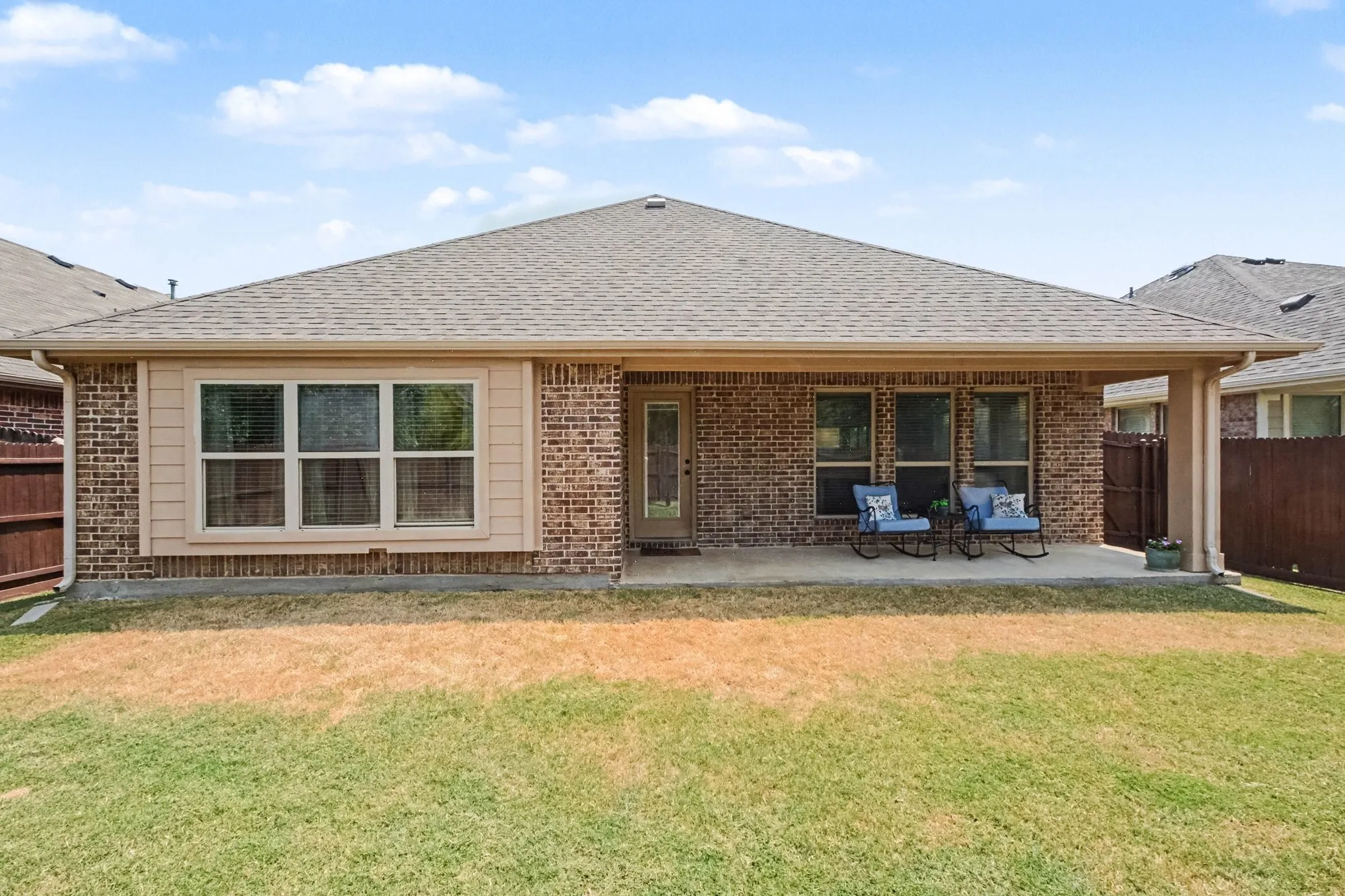 Expansive backyard with a covered patio, brick exterior, multiple windows, a rear entry door, and a shingled roof