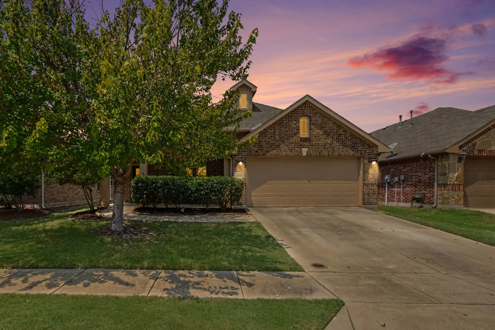 Brick and stone exterior featuring an attached two-car garage, concrete driveway, and manicured landscaping