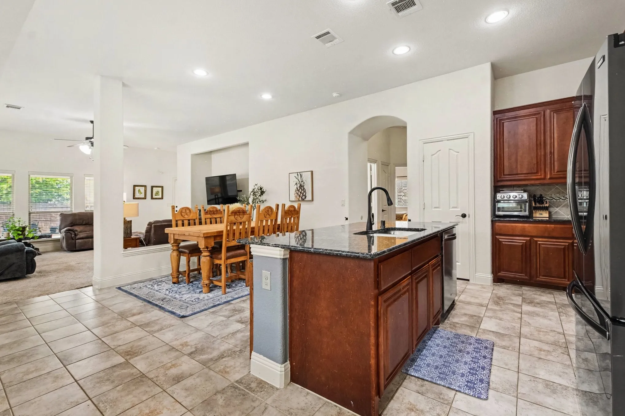 Kitchen featuring tile flooring, dark wood cabinetry, a granite countertop island with an integrated sink, a black faucet, and stainless steel appliances