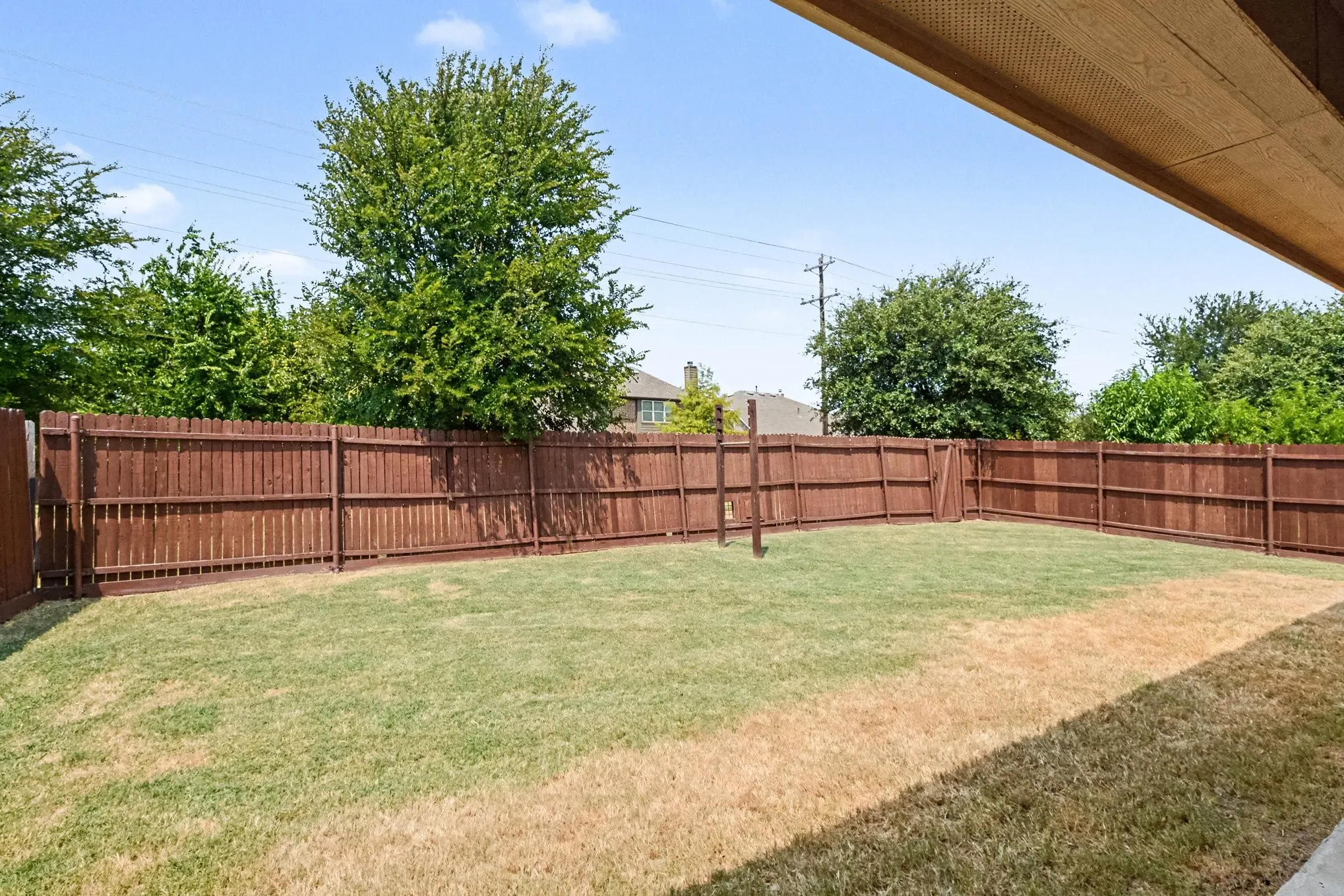 Spacious backyard featuring a full privacy fence, a grass lawn, and mature perimeter trees