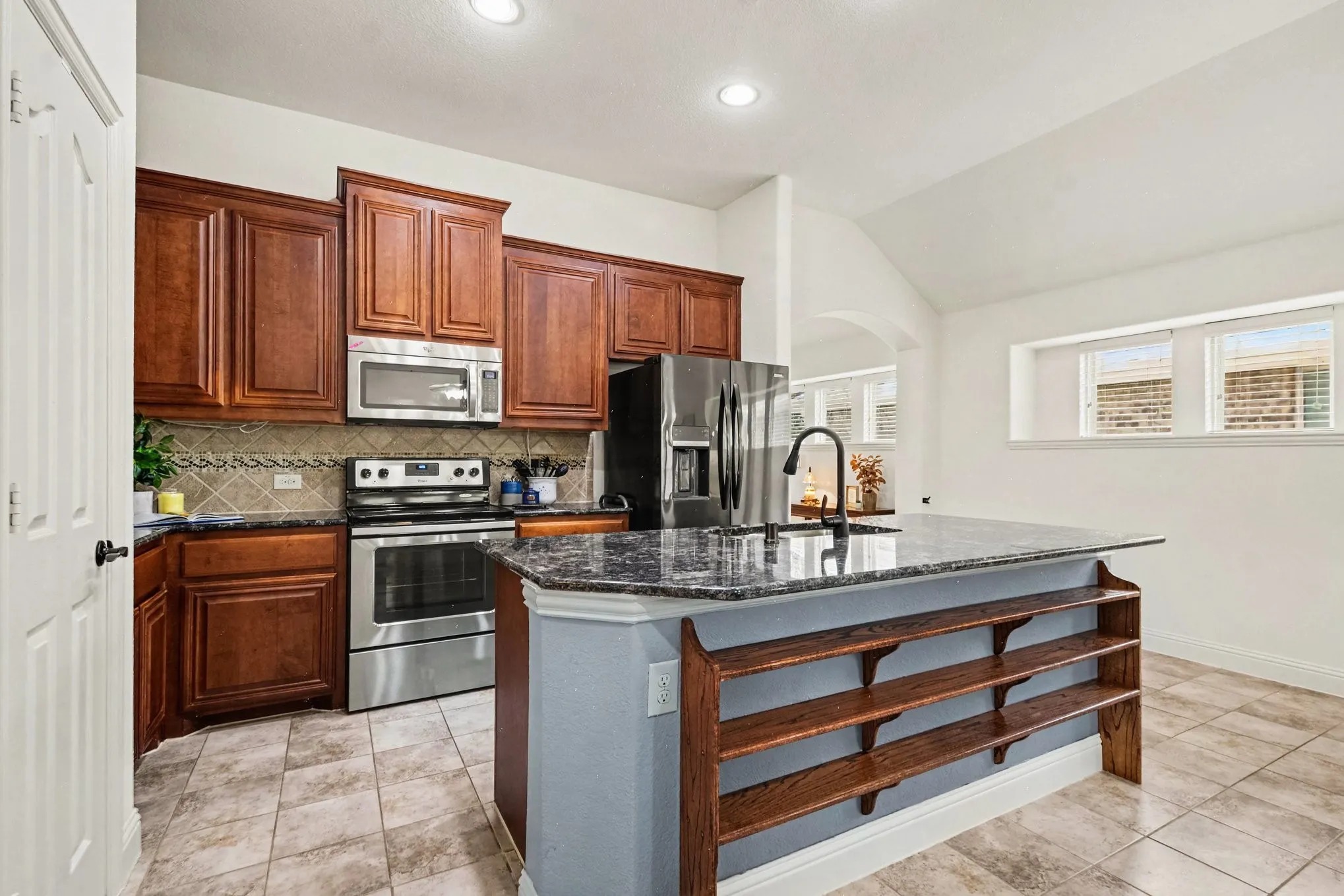 Kitchen featuring wood cabinetry, stainless steel appliances, a tiled backsplash, and an island with built-in shelving