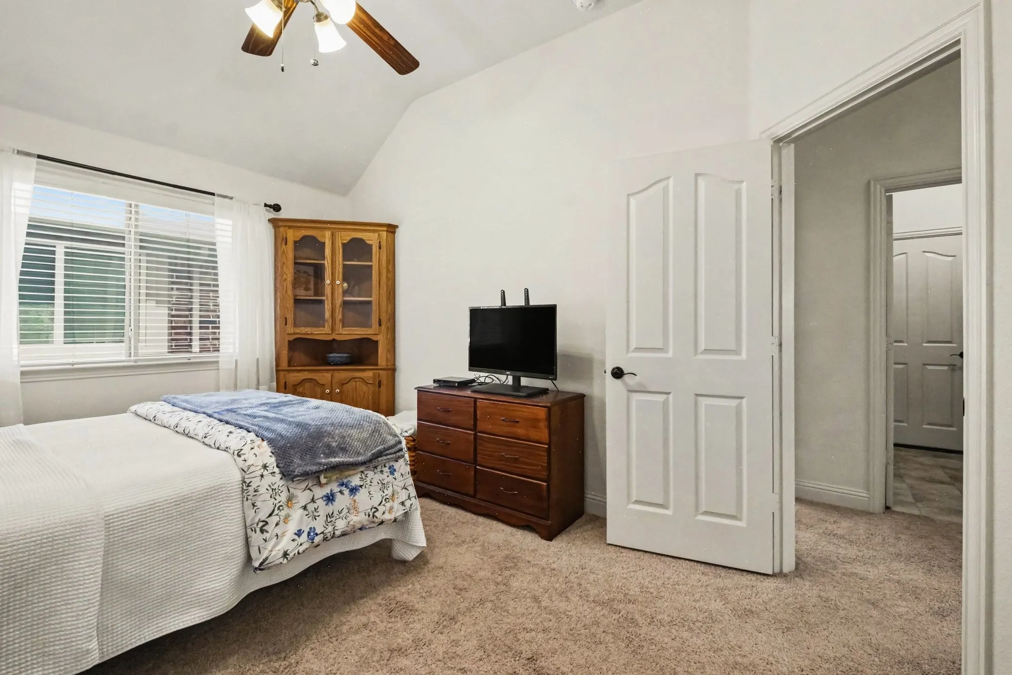 Vaulted ceiling with a ceiling fan, window with blinds, paneled interior door, and carpet flooring