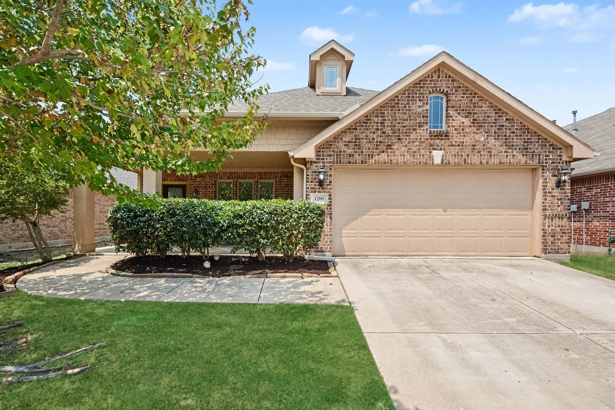 Brick and siding exterior featuring a covered entry, attached two-car garage, and established landscaping