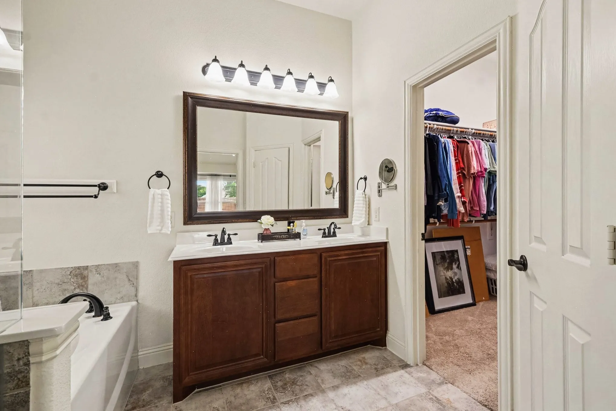 Dual vanity with wood-finish cabinetry, built-in bathtub, and an adjacent walk-in closet