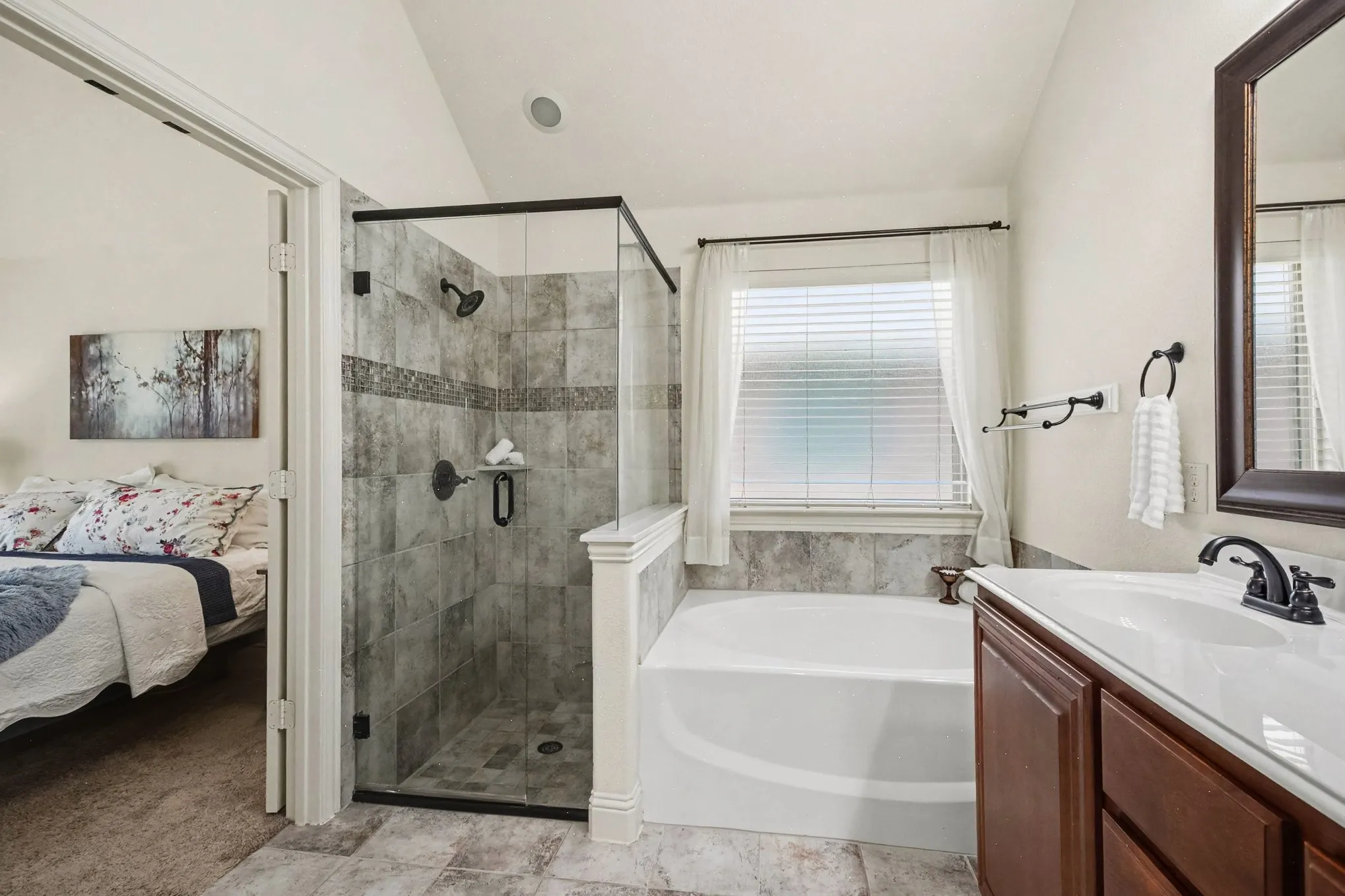 Glass-enclosed shower with tile surround and decorative accent band, separate soaking tub, and single vanity with solid surface countertop
