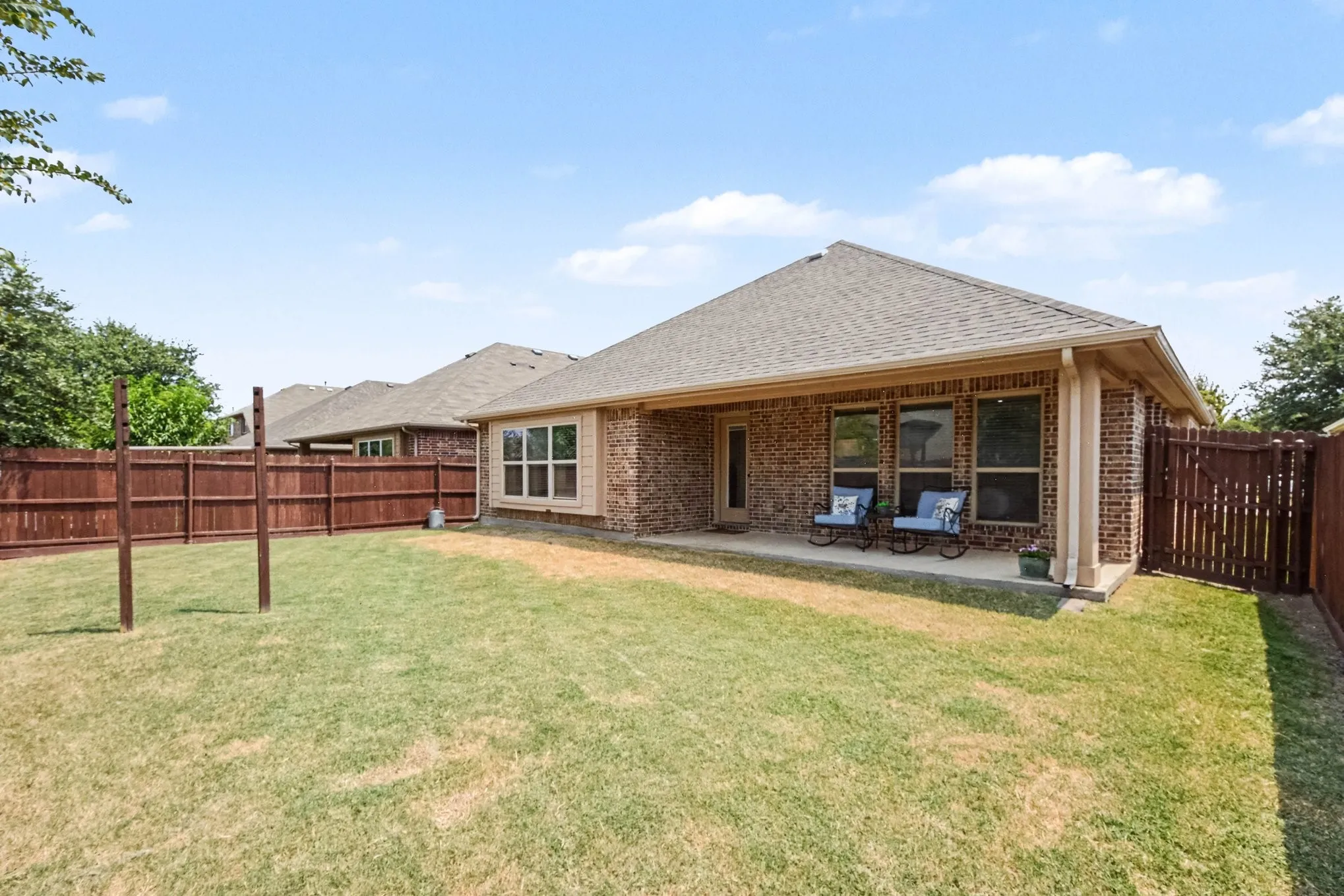 Expansive backyard featuring a manicured lawn with mature landscaping, wood privacy fencing, and a covered patio area