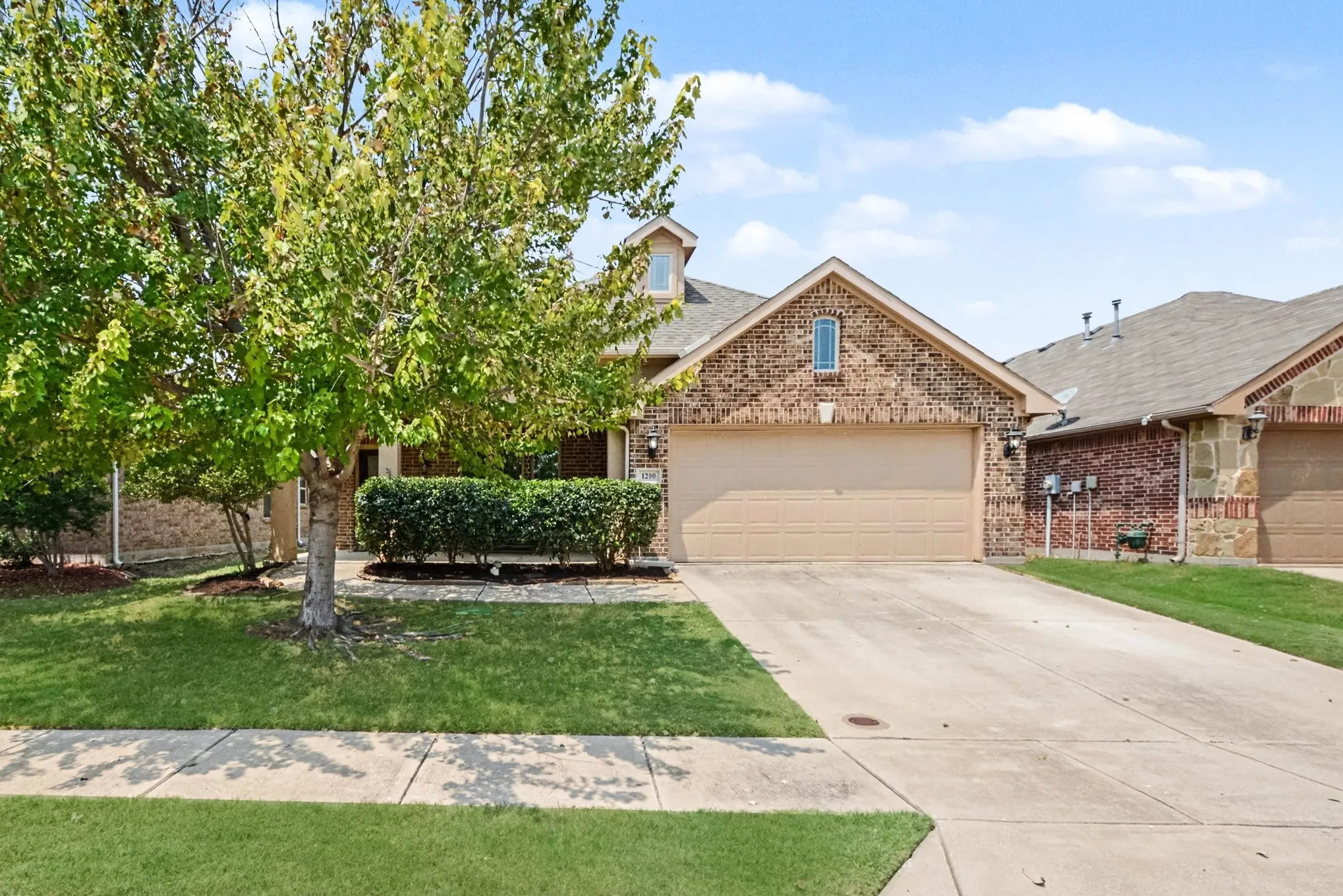 Brick exterior with stone accents, an attached garage, a concrete driveway, a manicured lawn, and mature trees