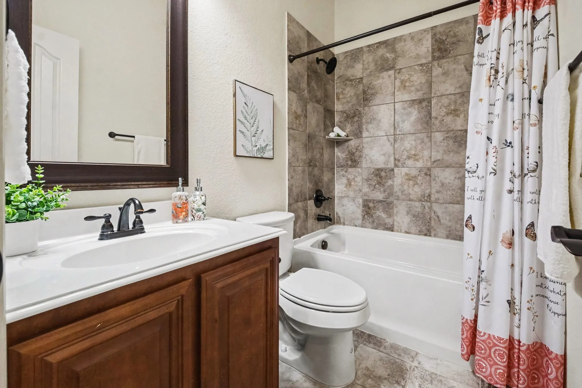 Bathroom featuring a wood-finish vanity with an integrated sink, framed mirror, and a tub-shower combination with tiled surround