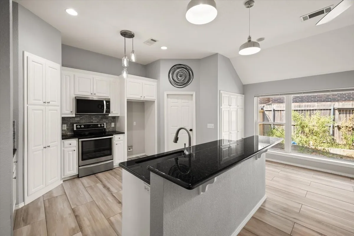 Kitchen featuring white cabinetry, black stone countertops, stainless steel appliances, and a tile backsplash