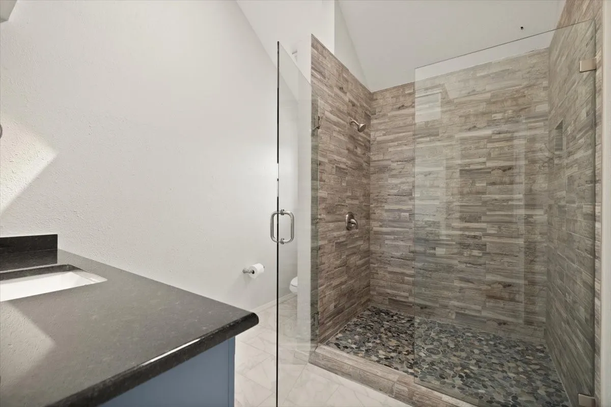 Glass-enclosed shower with pebble-finish flooring and stacked stone-look wall tiling
