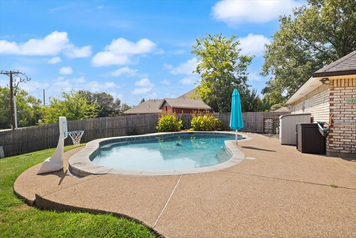 Curved swimming pool with stone coping, surrounded by an exposed aggregate concrete patio
