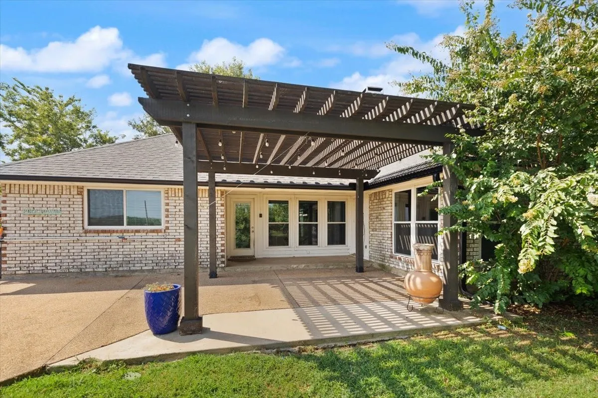 Expansive patio featuring a dark wood pergola, concrete surfacing, and a white brick exterior