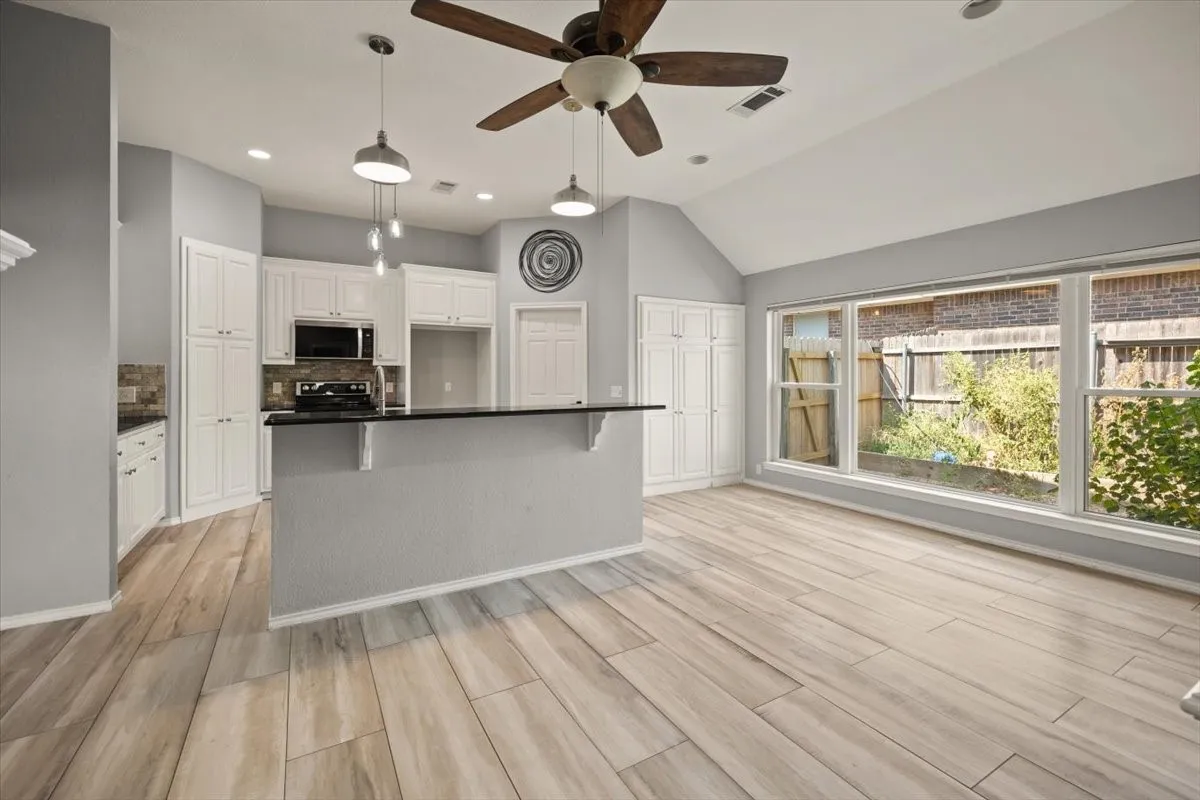 Vaulted ceiling with a ceiling fan, white cabinetry, dark countertops, wood-finish flooring, and multiple large windows