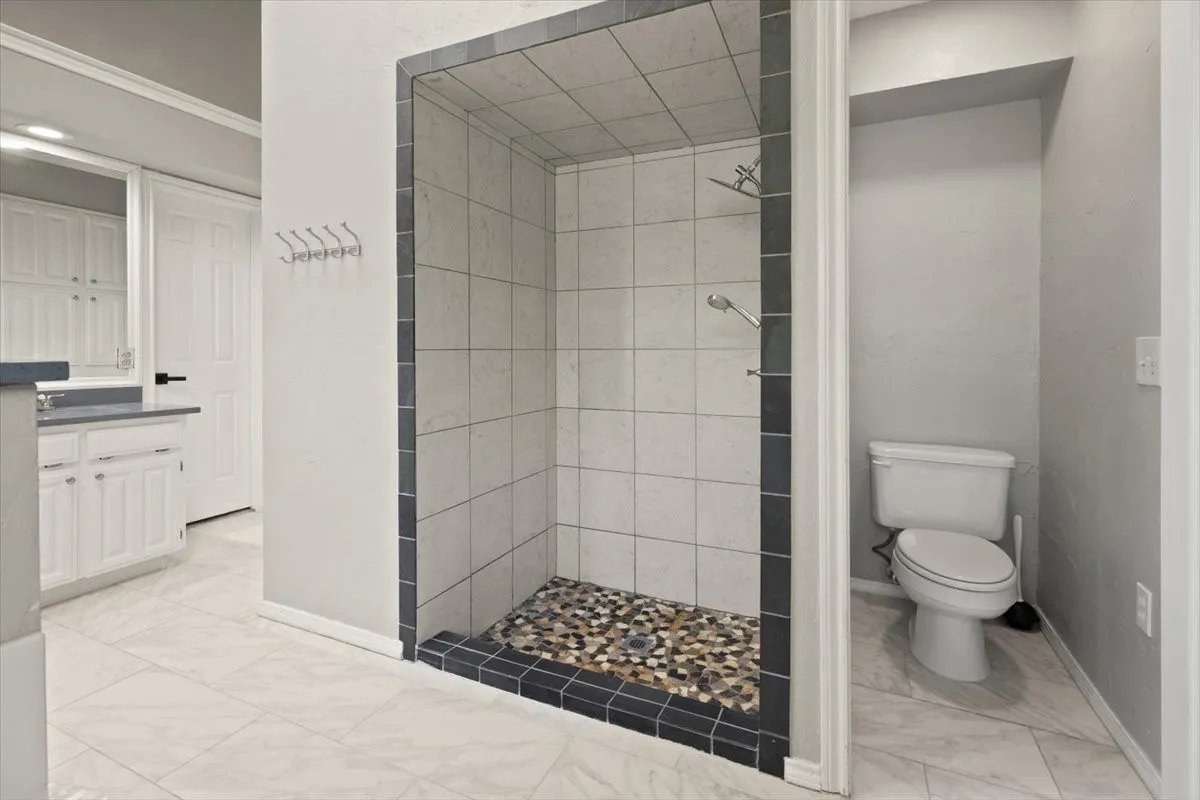 Walk-in shower with pebble tile floor and square wall tiling, complemented by white tile flooring, a white vanity with hardware, and built-in white cabinetry