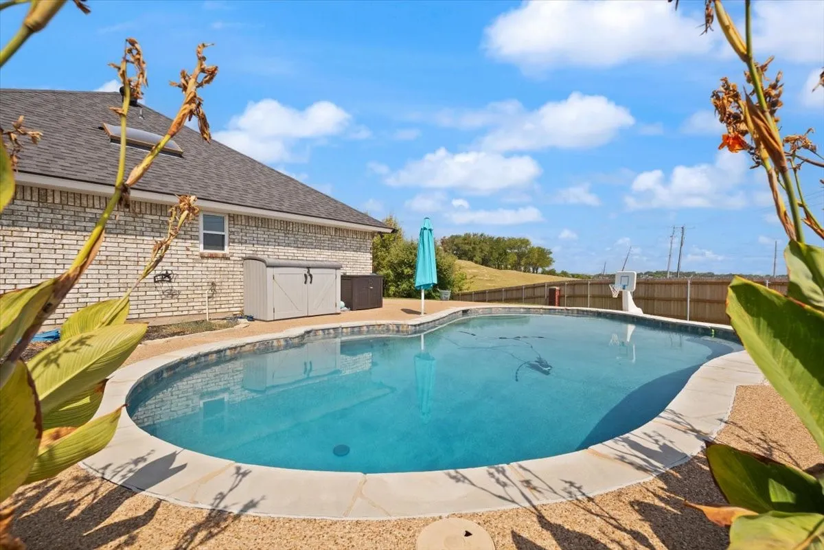 Freeform swimming pool with a surrounding aggregate deck, complemented by a brick exterior and a privacy fence
