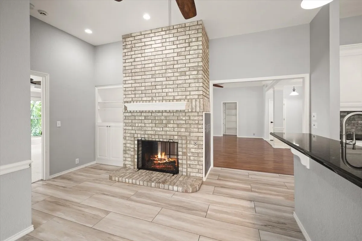 Brick fireplace with a white mantel, built-in shelving, wood-finish flooring, and a kitchen counter with a dark countertop