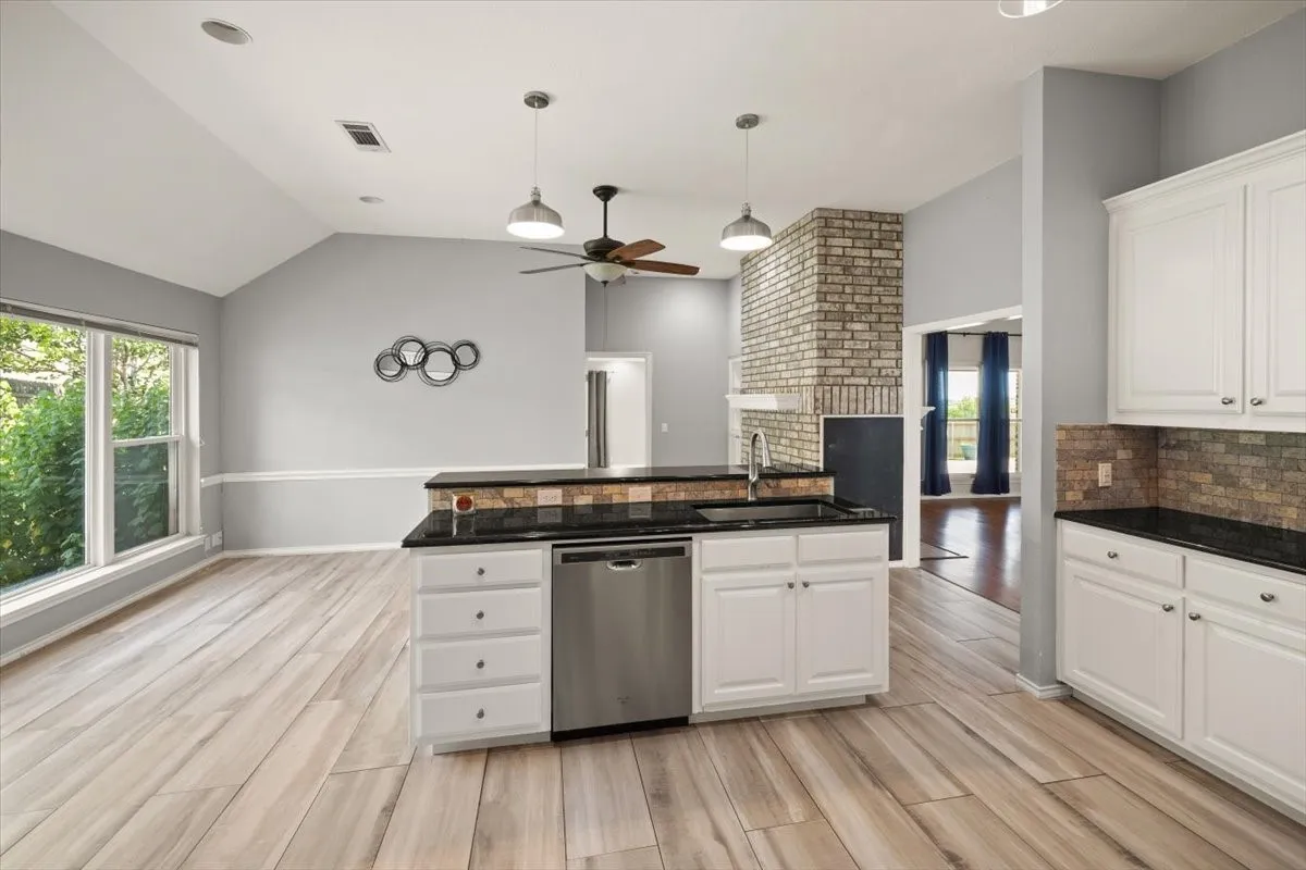 Kitchen featuring wood-finish flooring, an island with a stainless steel dishwasher, white cabinetry, black countertops, and a stone tile backsplash