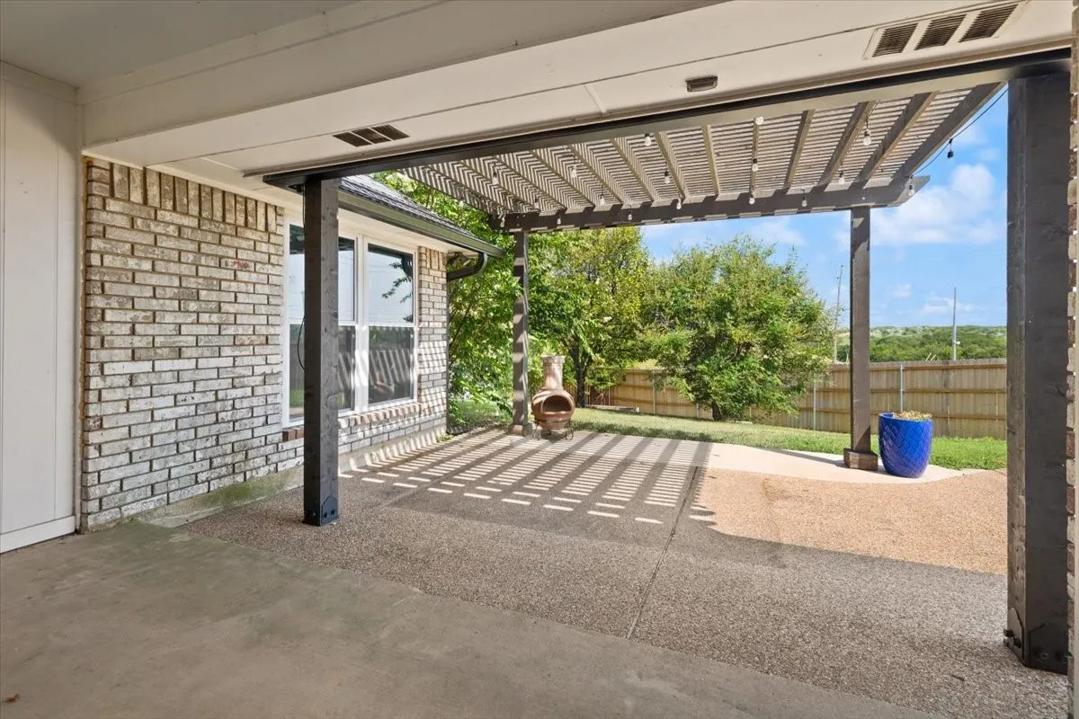 Covered patio with a slatted pergola, exposed aggregate concrete, and a brick exterior