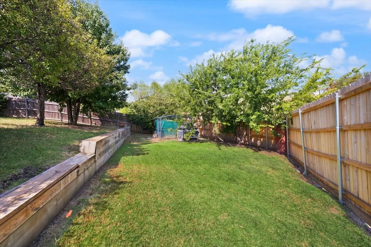 Expansive backyard featuring a manicured lawn, established trees, and wood fencing