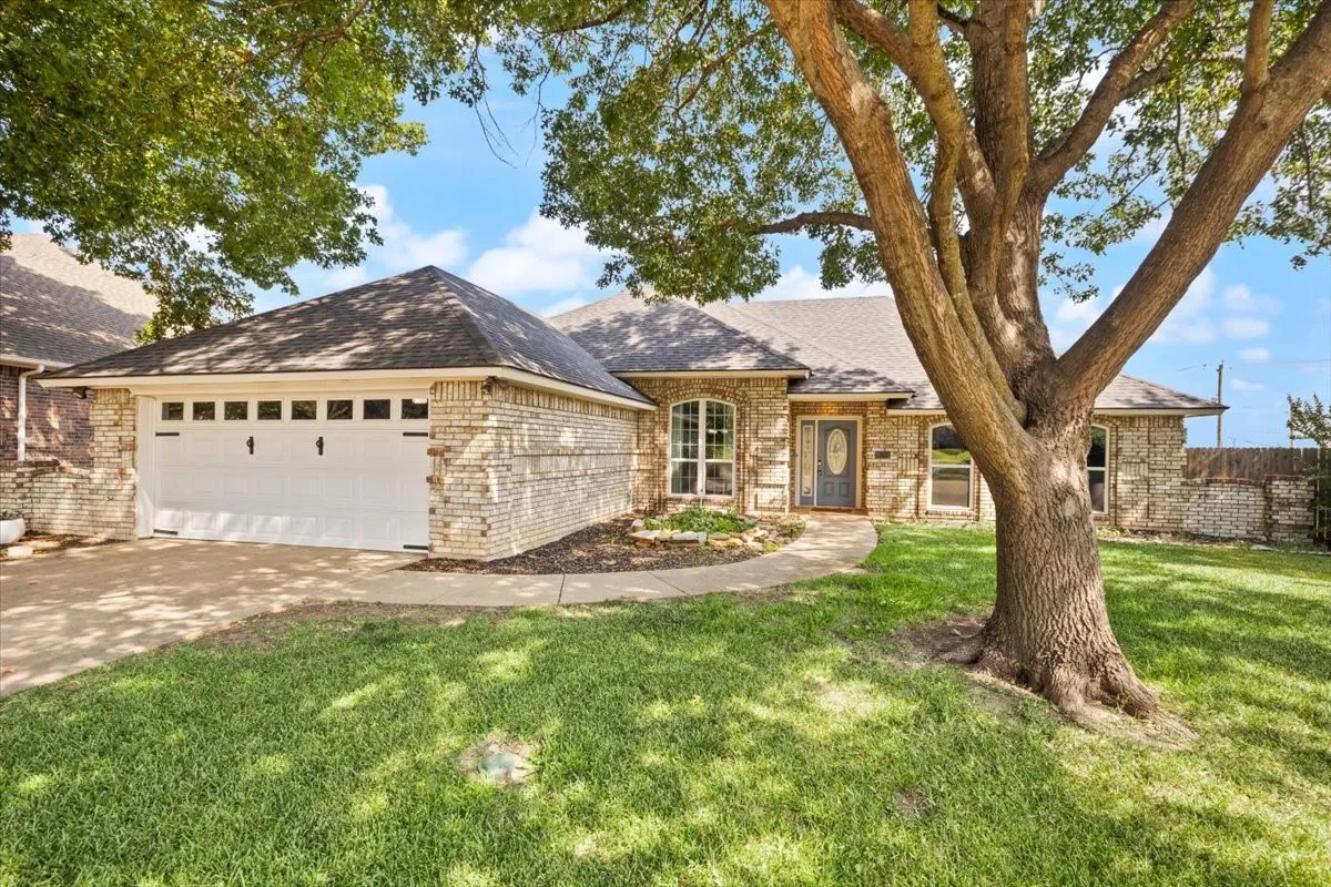 Brick exterior with arched windows, a two-car garage, and a mature front yard tree