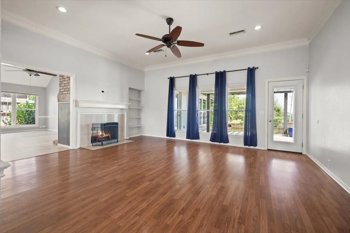 Wood-finish flooring, white mantel fireplace, built-in shelving, recessed lighting, and a ceiling fan