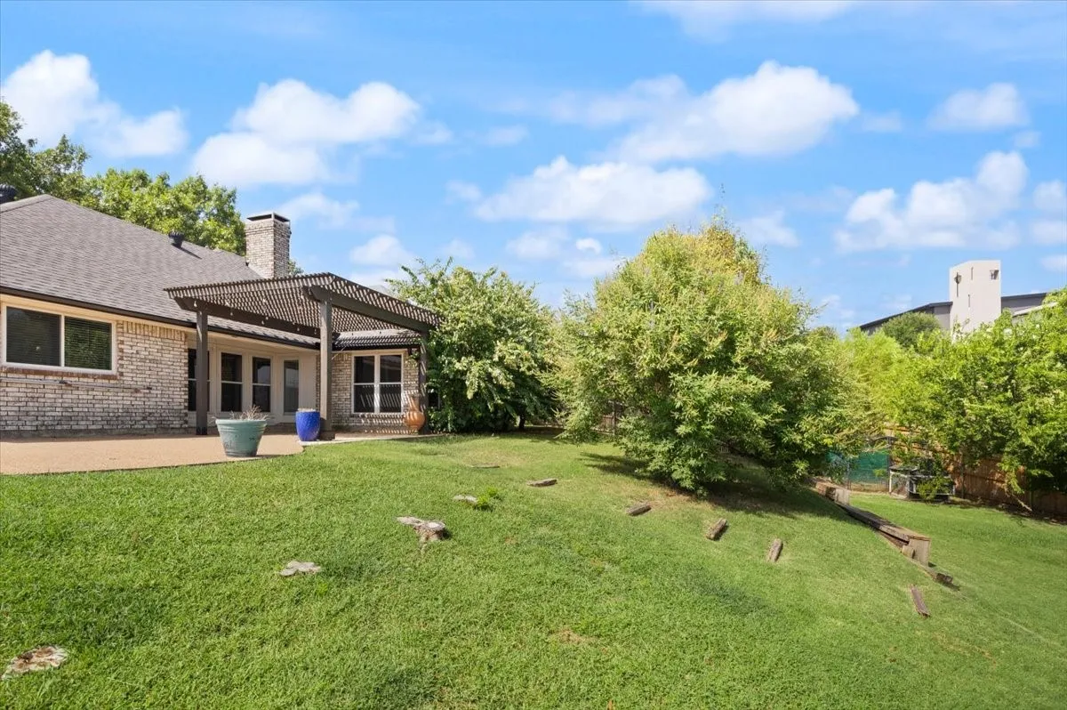 Expansive backyard featuring a manicured lawn, an attached patio with a pergola, and mature landscaping