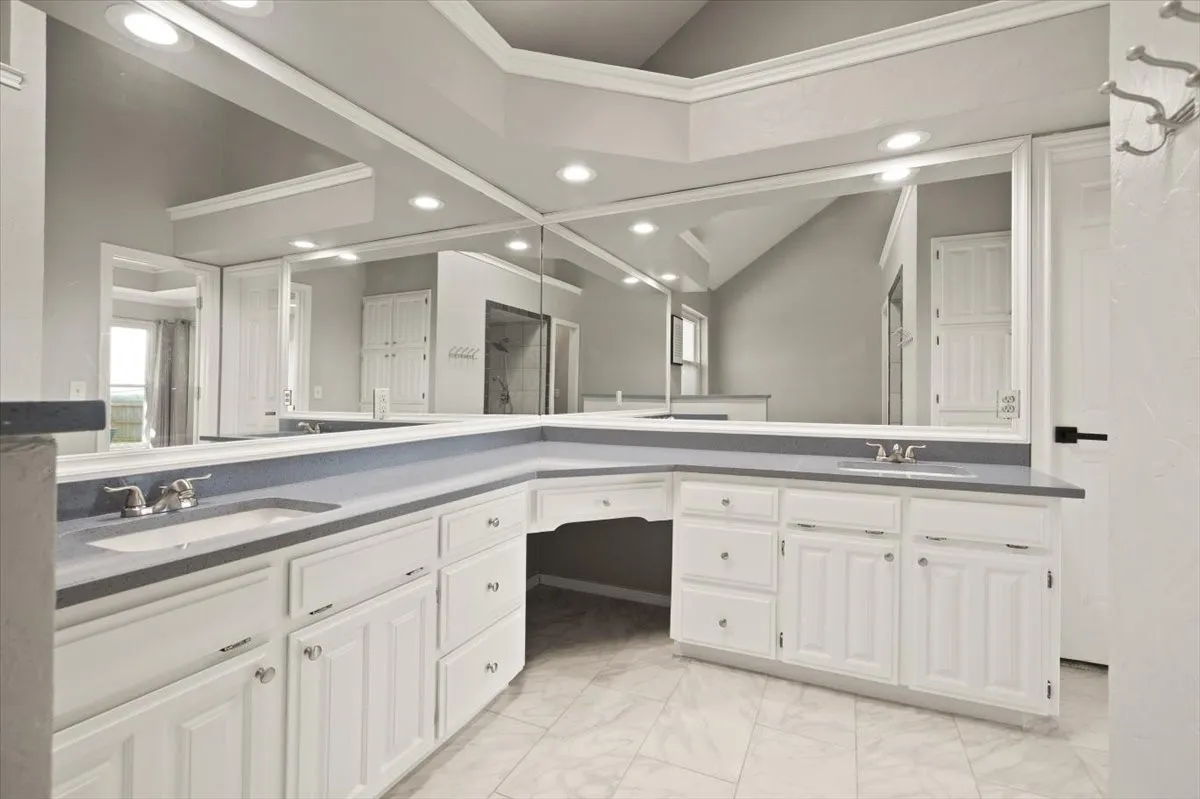 Dual vanity with integrated sinks and chrome fixtures, extensive mirrored wall, white cabinetry with silver-tone hardware, and tiled flooring