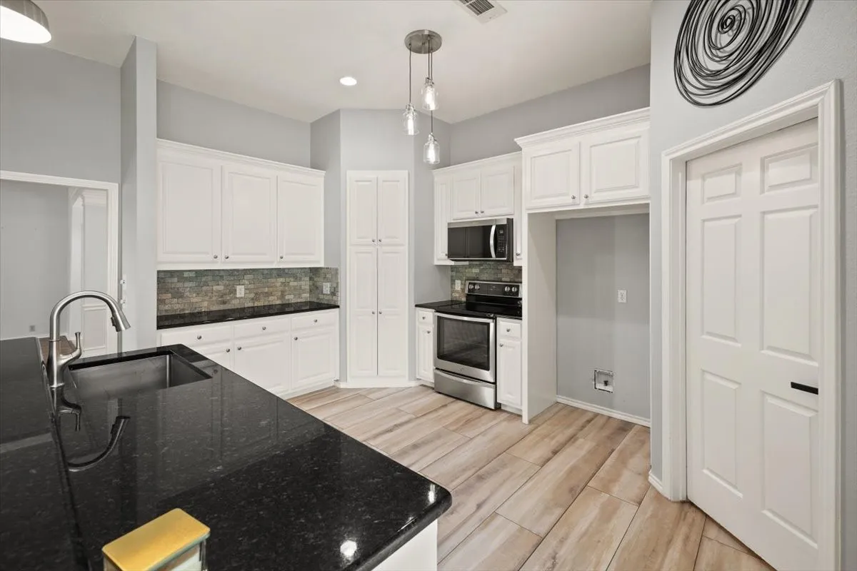Kitchen featuring wood-finish flooring, white cabinetry, black countertops, and stainless steel appliances