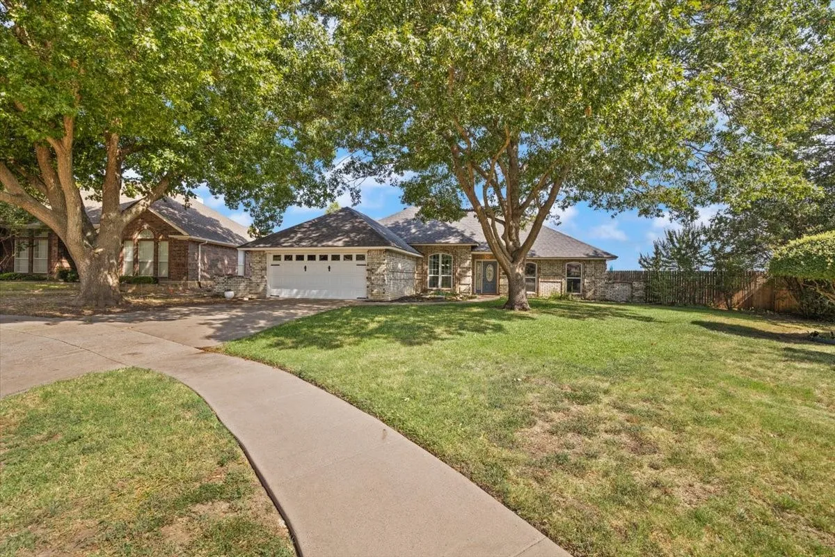 Stone and brick exterior with a two-car garage, mature trees, and a concrete walkway