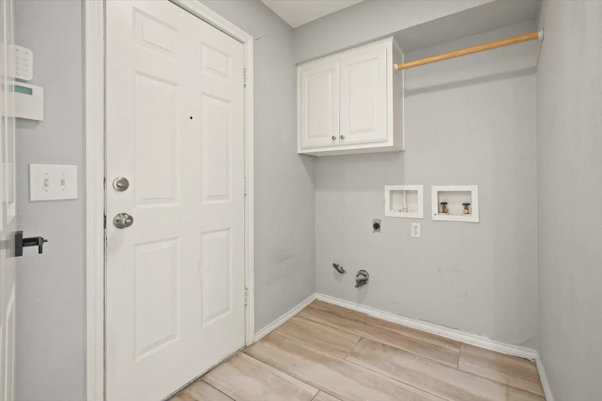 Laundry area with wood-finish flooring, white cabinetry, a hanging rod, and wall-mounted utility hookups
