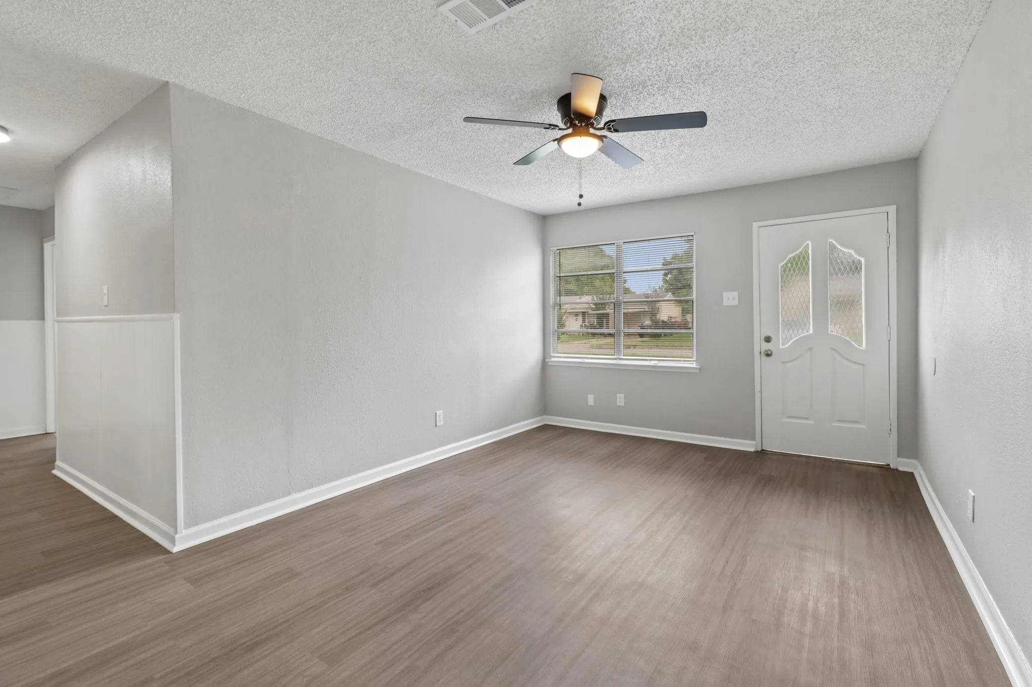 Wood-finish flooring, ceiling fan with integrated lighting, wall paneling, multi-pane window, and decorative front entry door