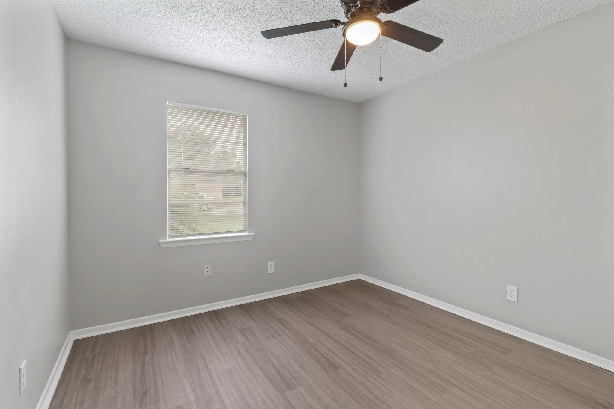 Neutral gray walls, wood-finish flooring, and a ceiling fan with integrated lighting