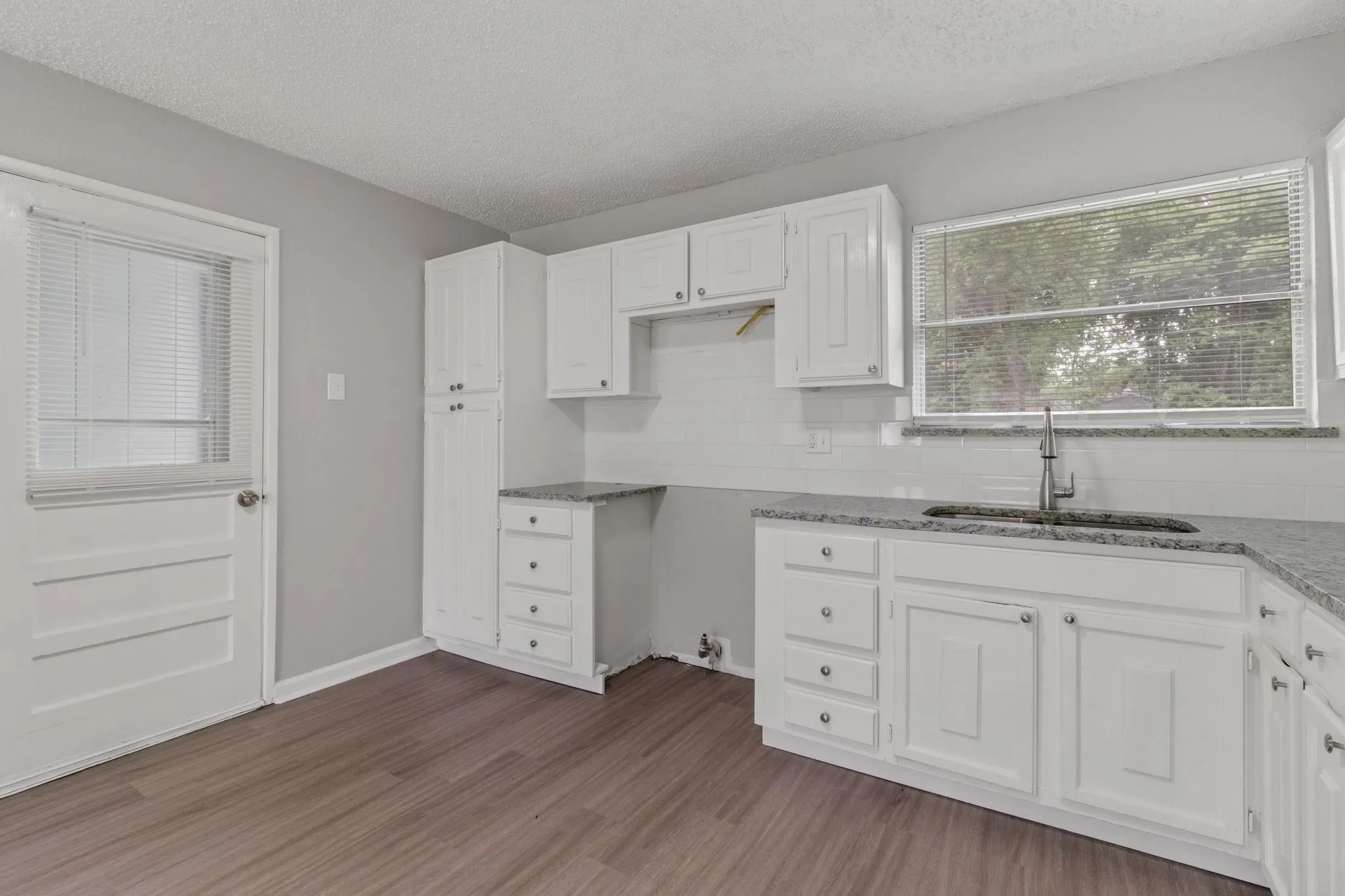 Kitchen featuring wood-finish flooring, white cabinetry, a large window, granite-style countertops, and a white subway tile backsplash