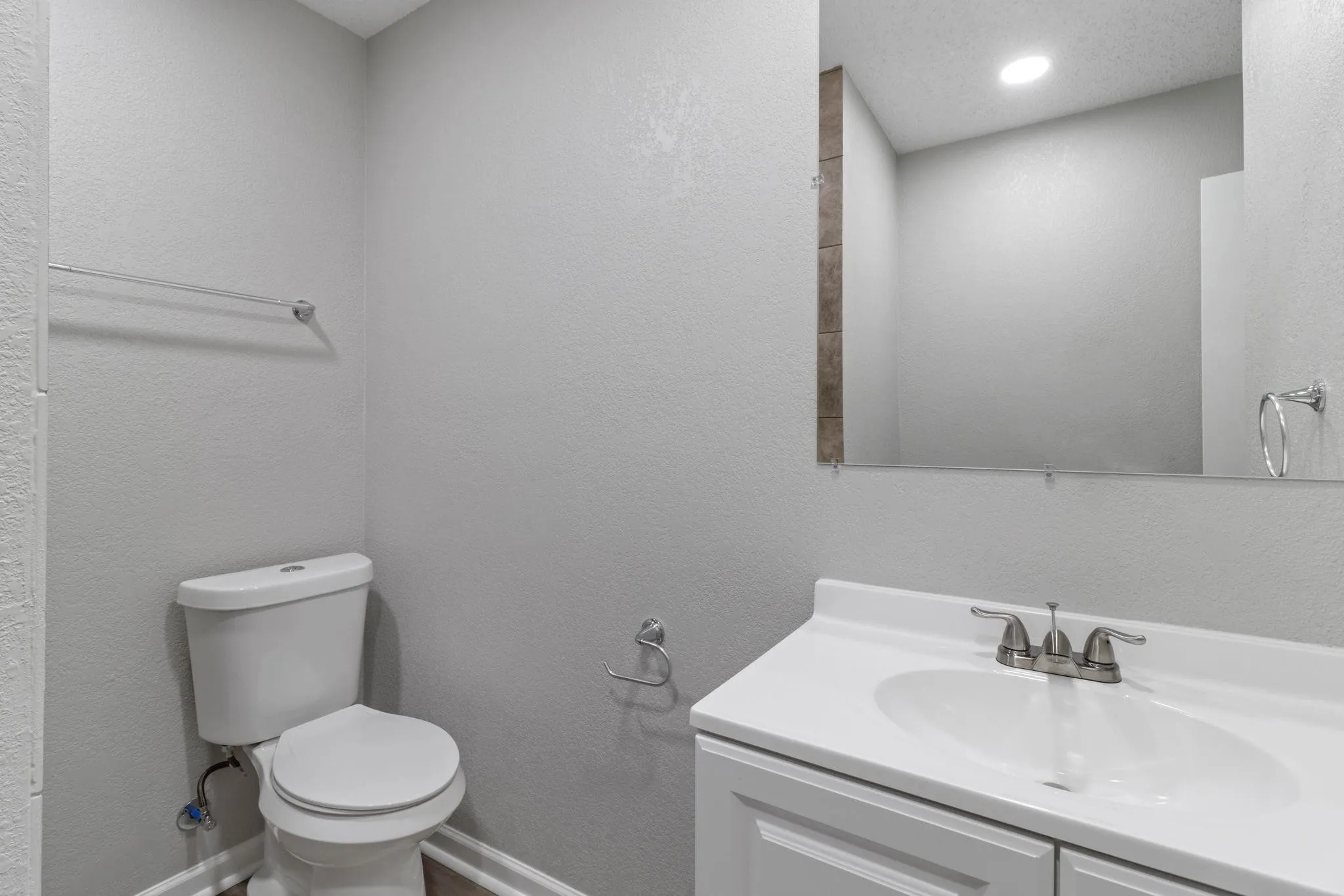 White vanity with integrated sink, mounted mirror, brushed nickel faucet, and a wall-mounted light fixture