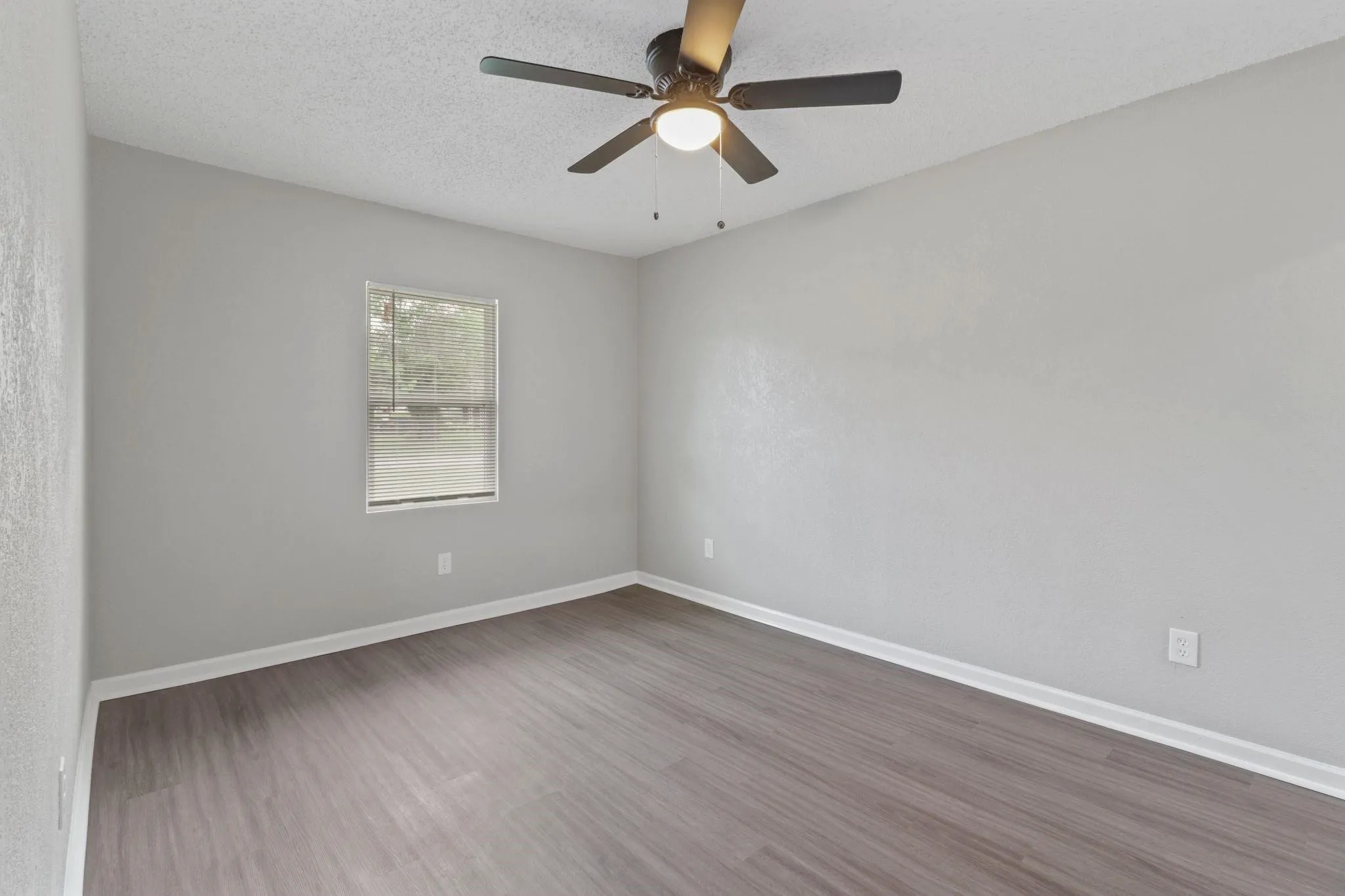 Wood-finish flooring, ceiling fan with integrated lighting, single window with blinds, light gray wall finish, white trim throughout
