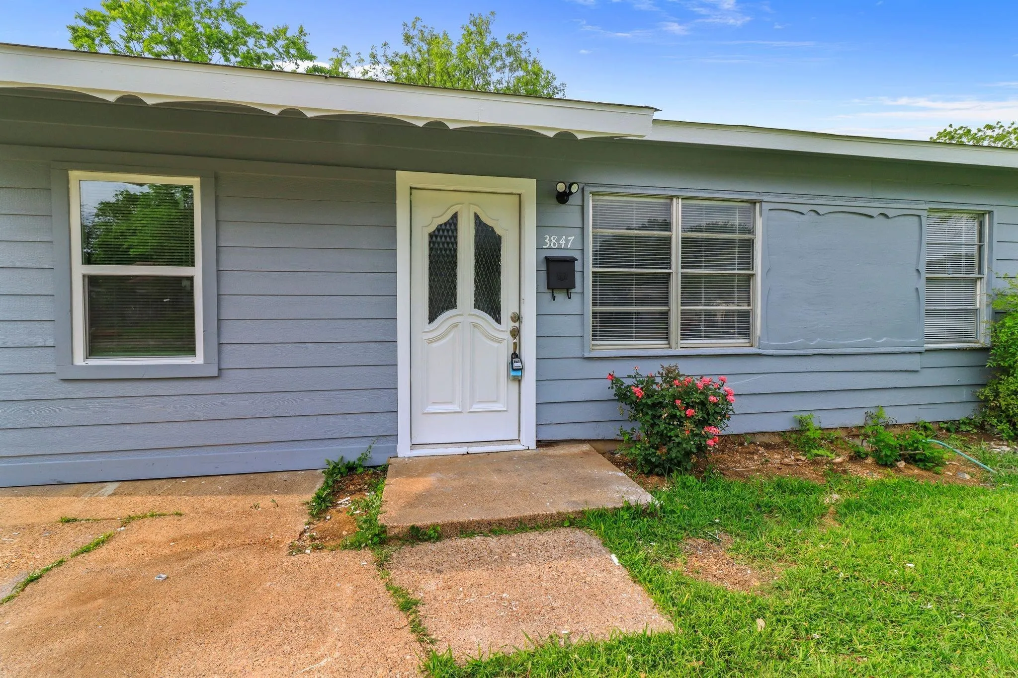 Front exterior featuring blue siding, white trim, a white entry door with glass inserts, and a concrete walkway