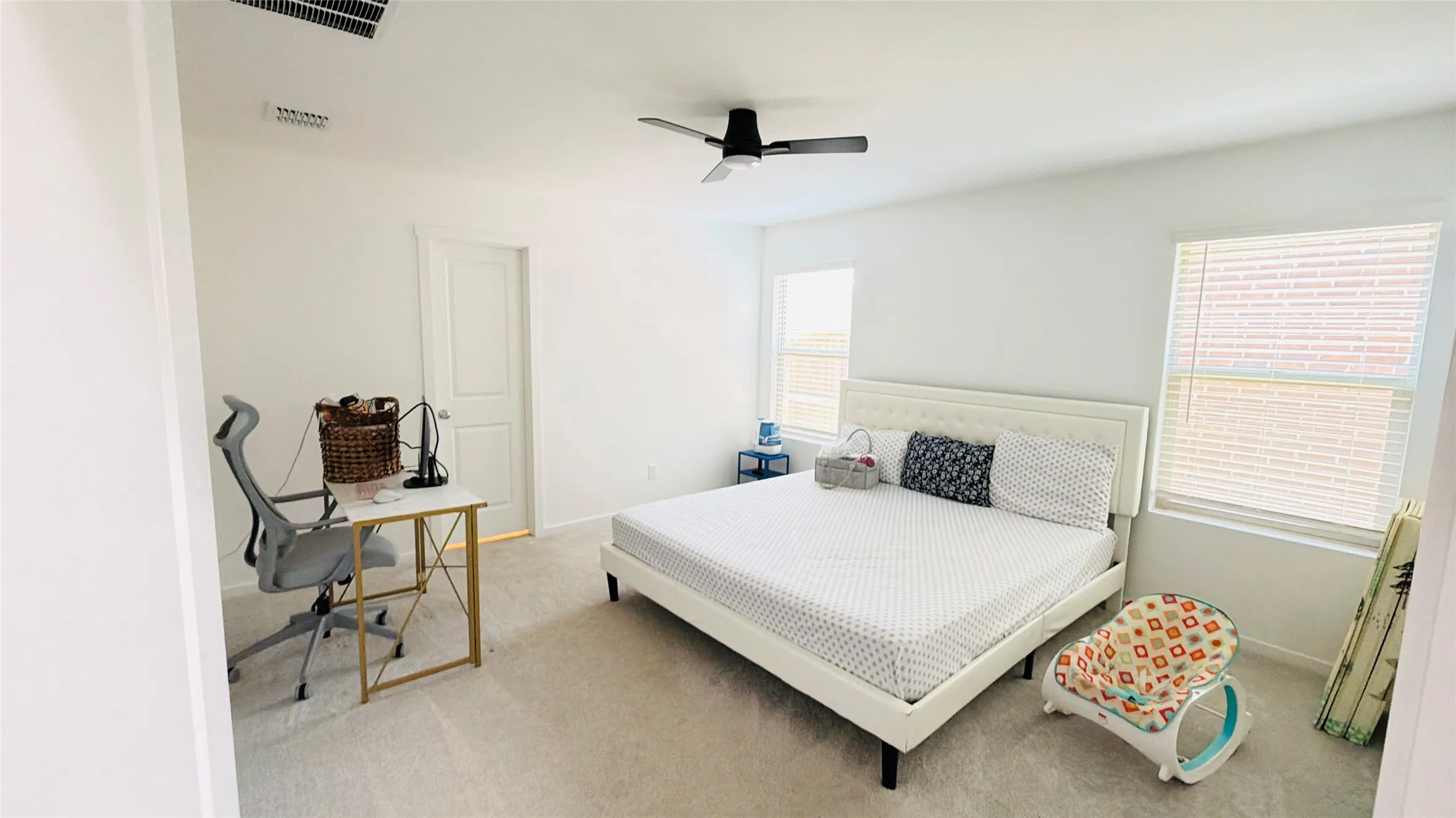Carpeted flooring, white walls, two windows with blinds, a ceiling fan, and an interior door