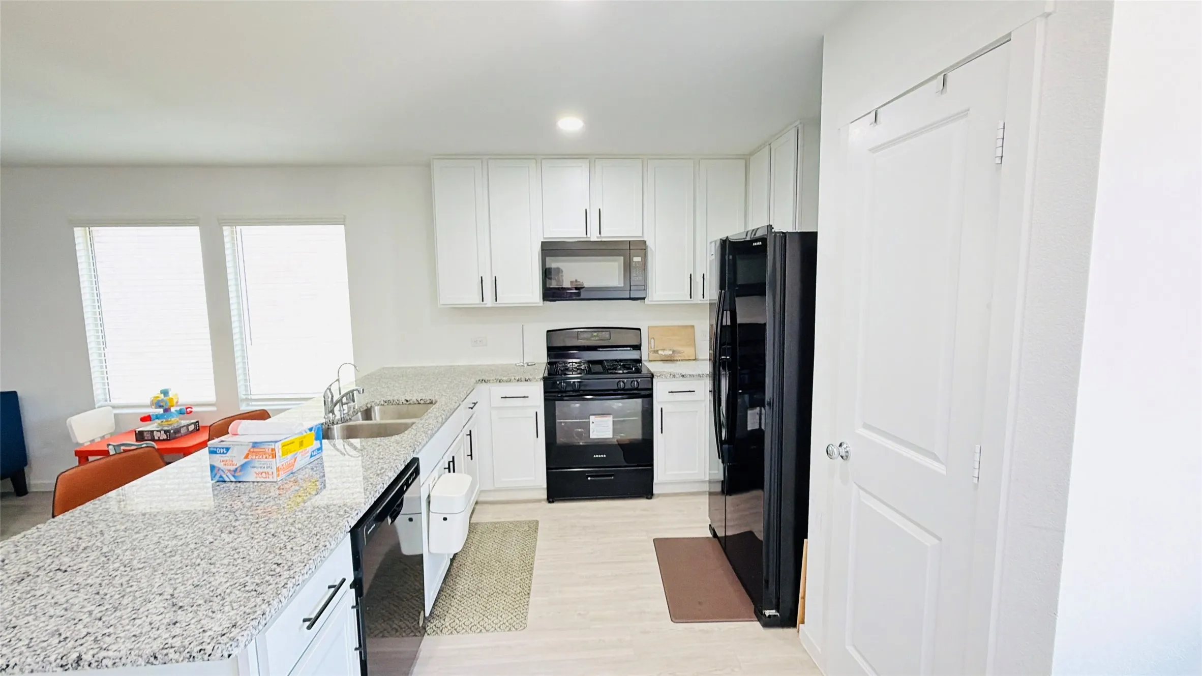 Kitchen featuring white cabinetry, light-toned flooring, black appliances, a double basin sink, and ample counter space with a light-colored speckled finish