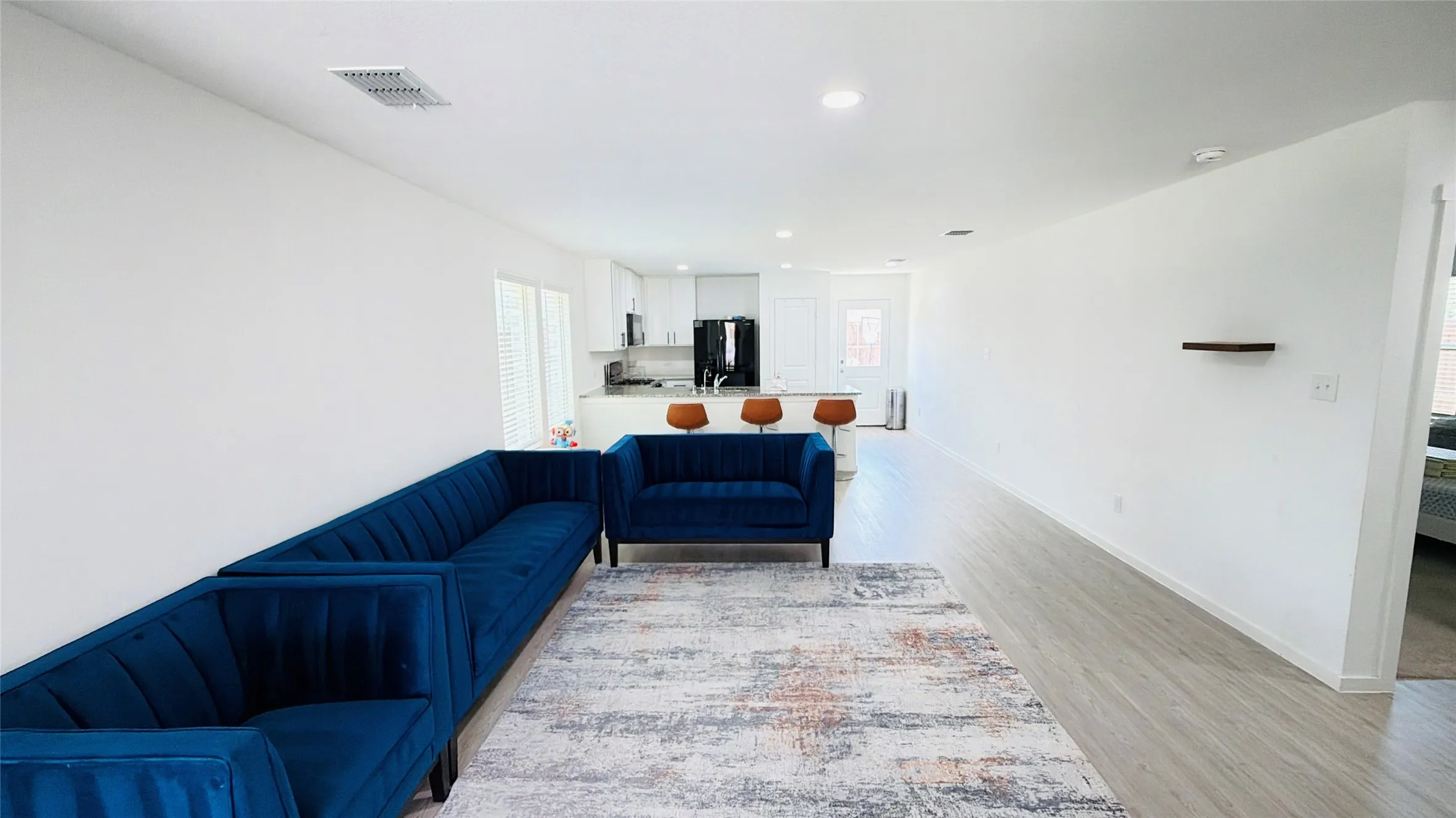 Open-concept living space featuring wood-finish flooring, recessed lighting, and a kitchen with white cabinetry and a black appliance suite