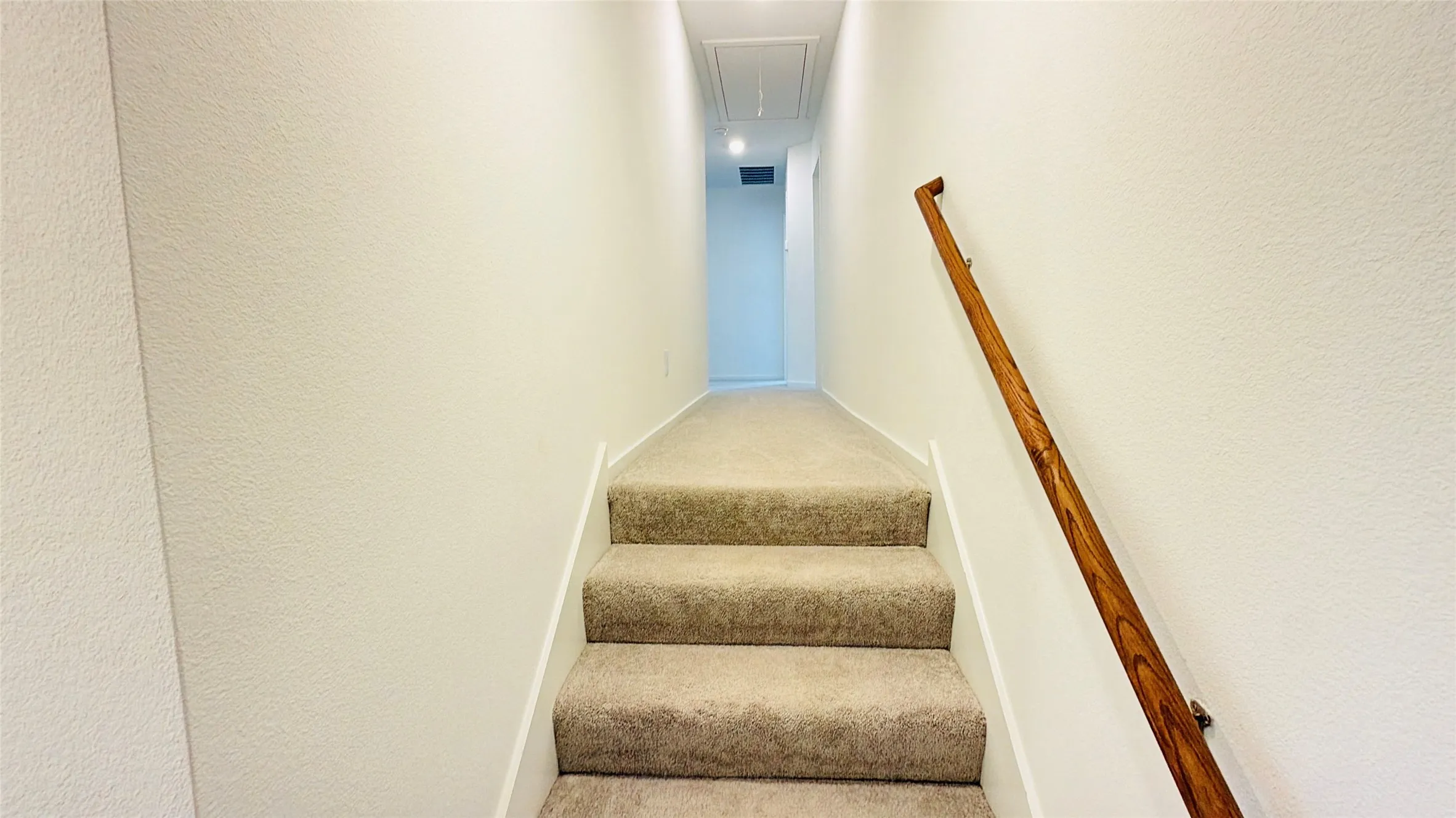 Carpeted staircase with a wood-finish handrail and light-colored walls