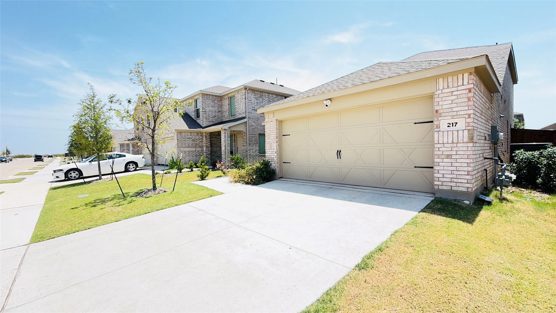 Light-colored brick exterior with a two-car garage, concrete driveway, and established front landscaping