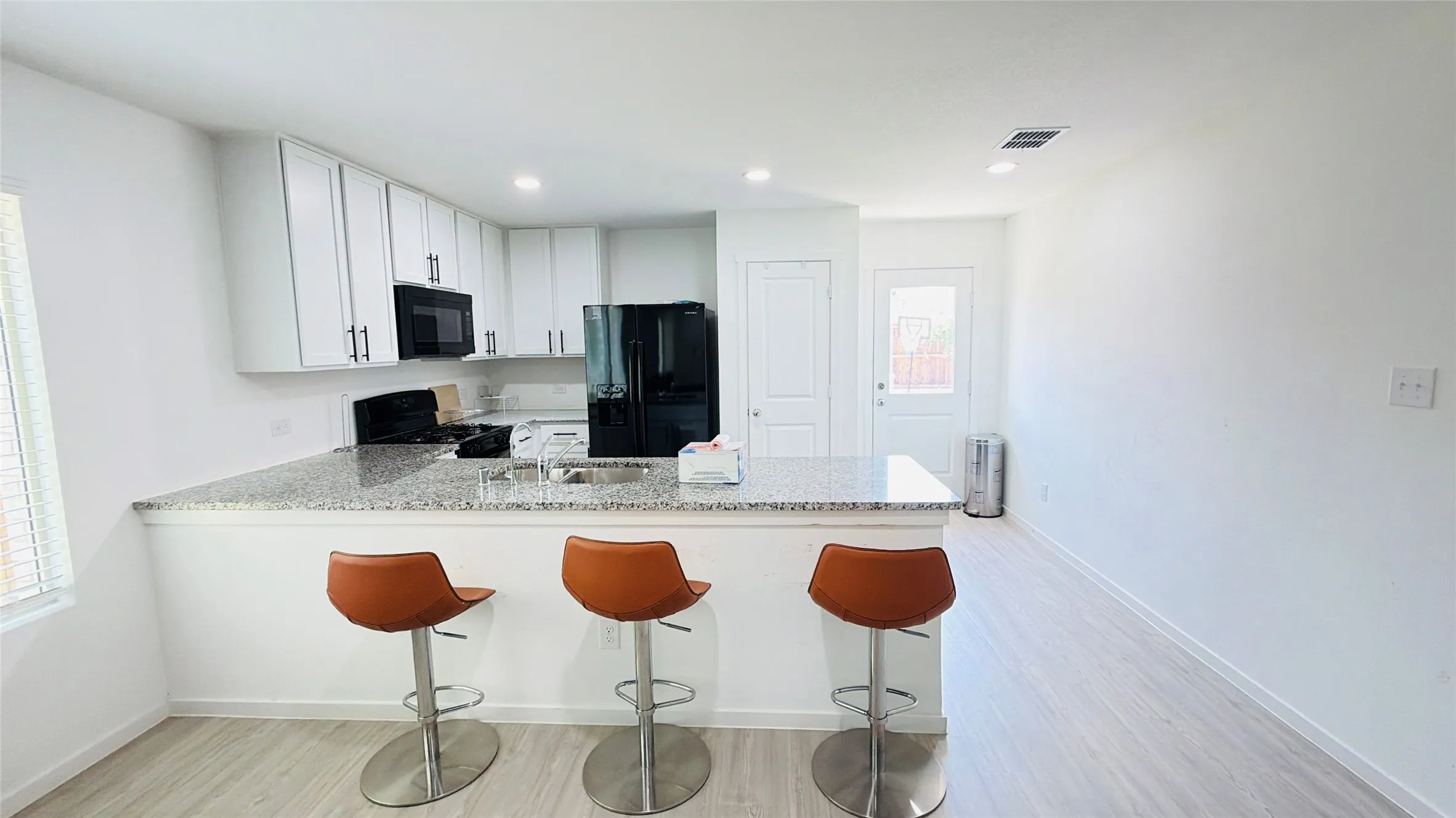 Kitchen featuring white cabinetry, black appliances, a stone countertop, and wood-finish flooring