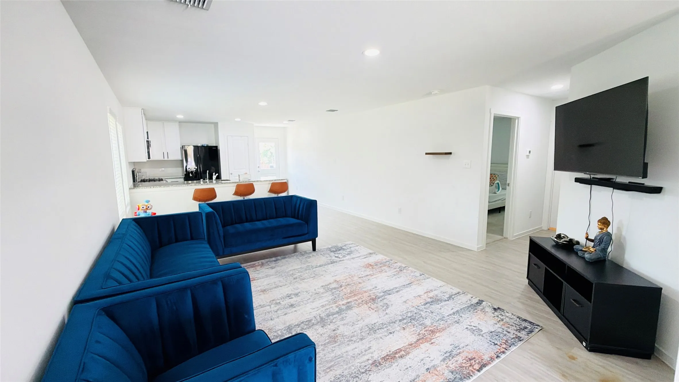 Open-concept living space featuring wood-finish flooring, recessed lighting, and a kitchen with white cabinetry, a built-in breakfast bar, and a black appliance package
