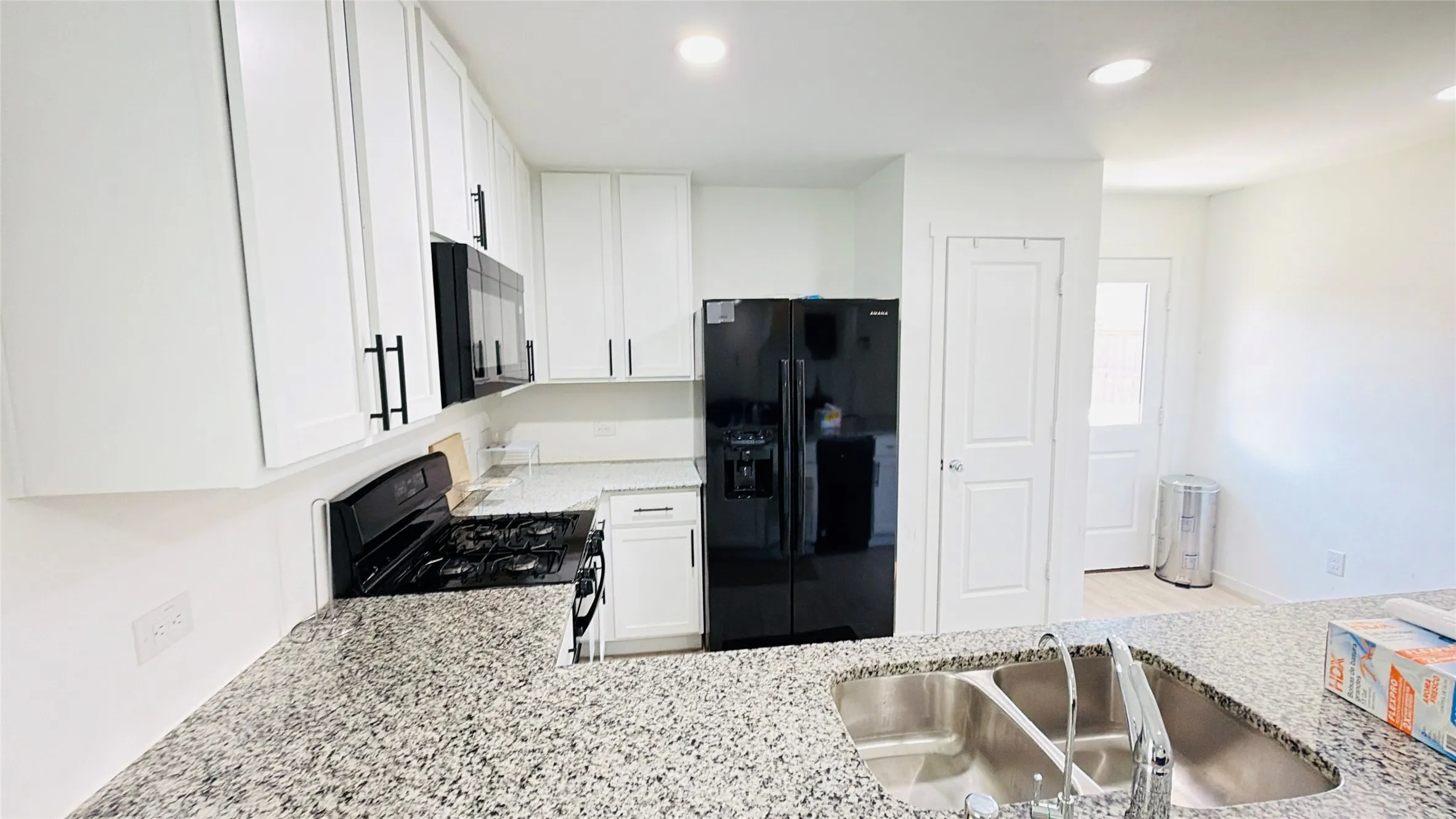 Spacious kitchen featuring granite countertops, white cabinetry with black hardware, black appliance suite, and a double basin stainless steel sink