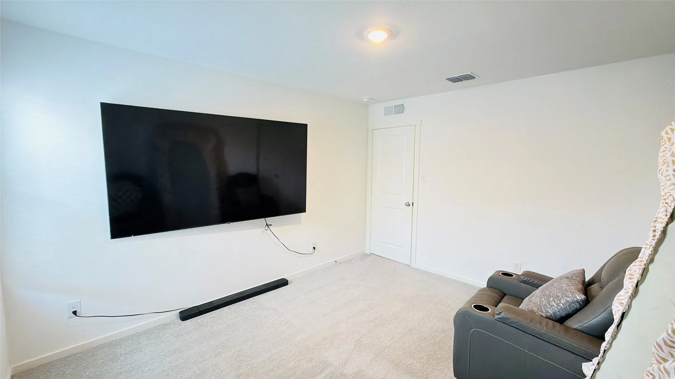 Neutral wall color, wall-mounted television, recessed ceiling light, and light-toned carpet flooring