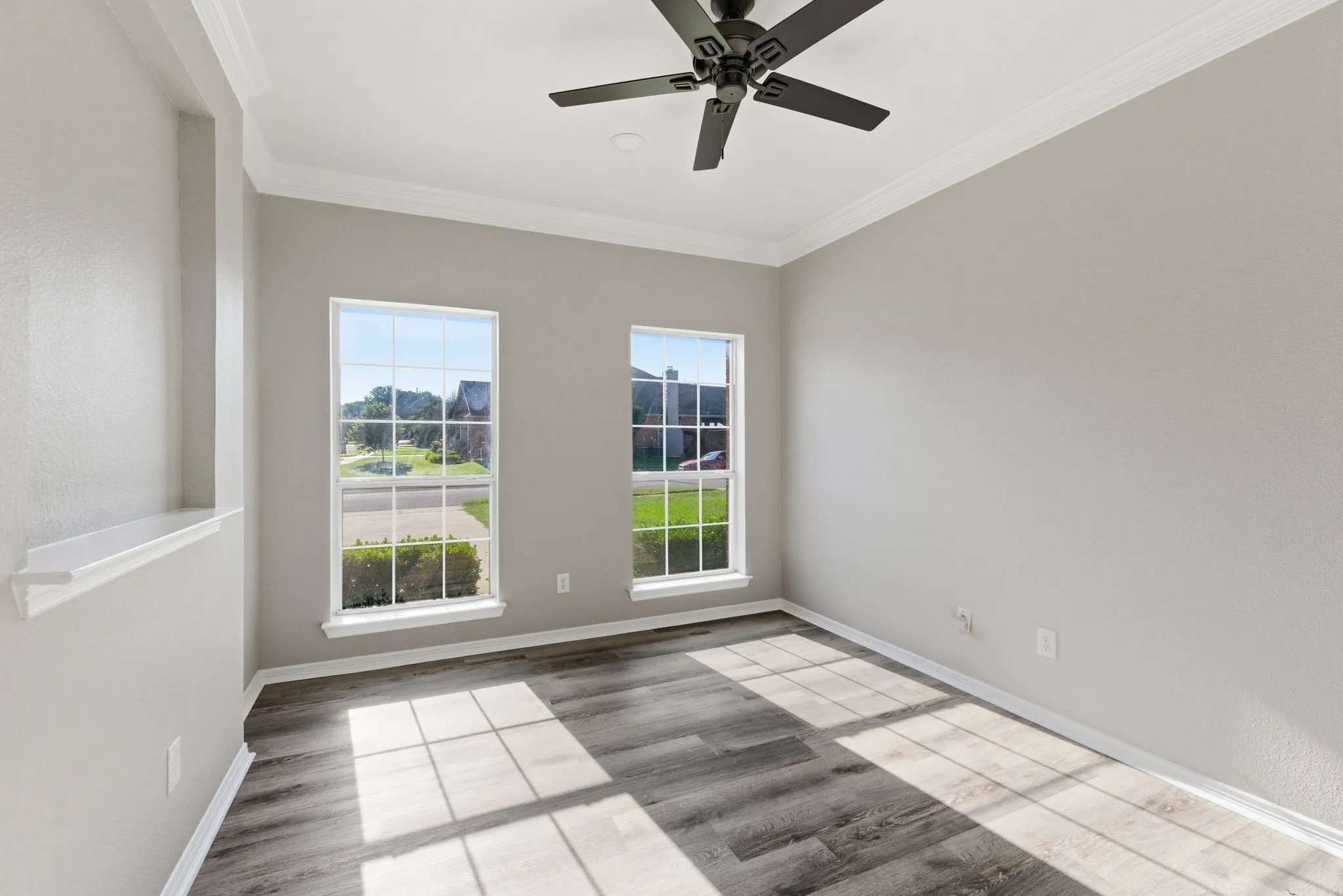 Room featuring wood-finish flooring, two large windows, crown molding, and a ceiling fan with integrated lighting