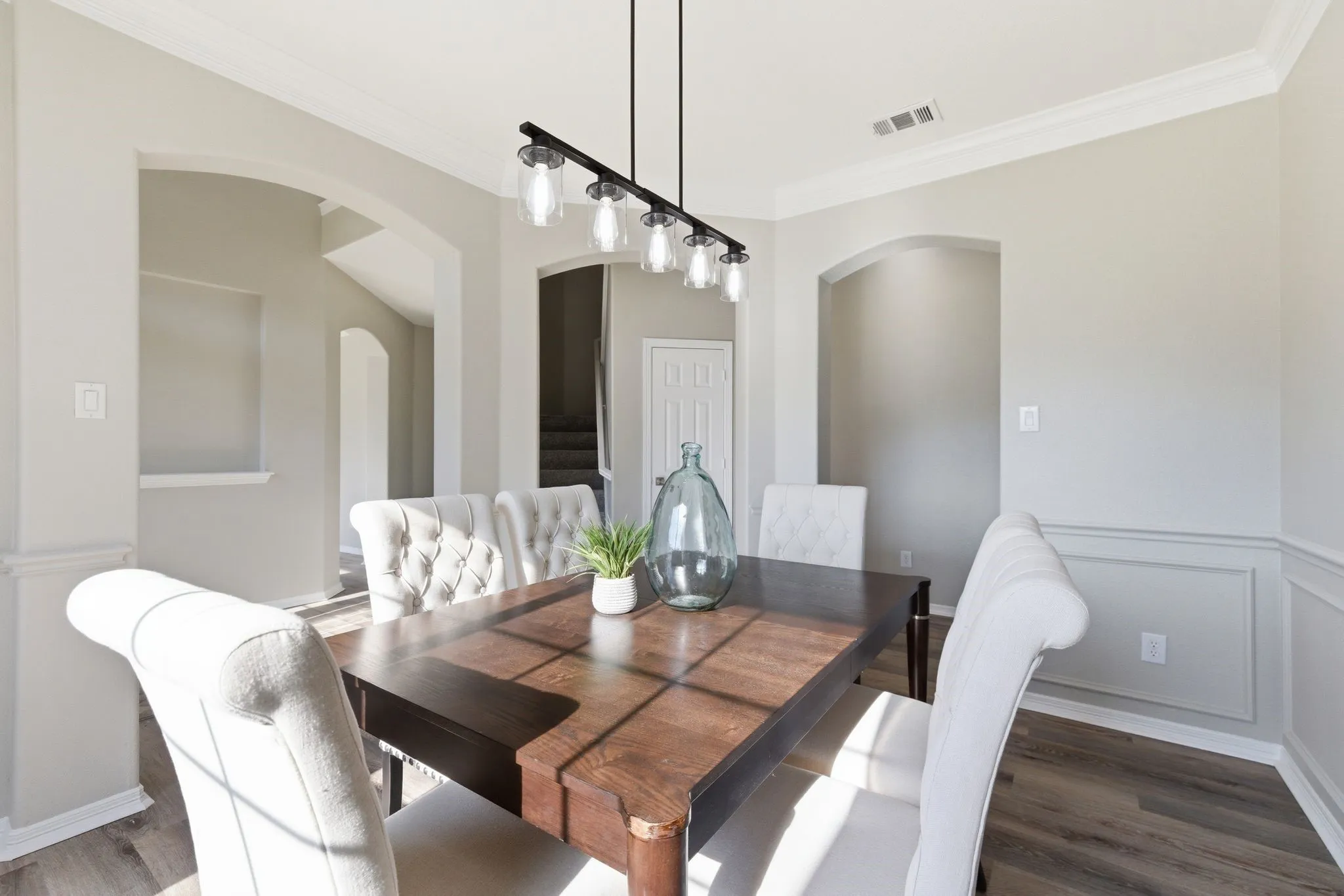 Dining area featuring a modern linear chandelier, crown molding, arched doorways, and wood-finish flooring