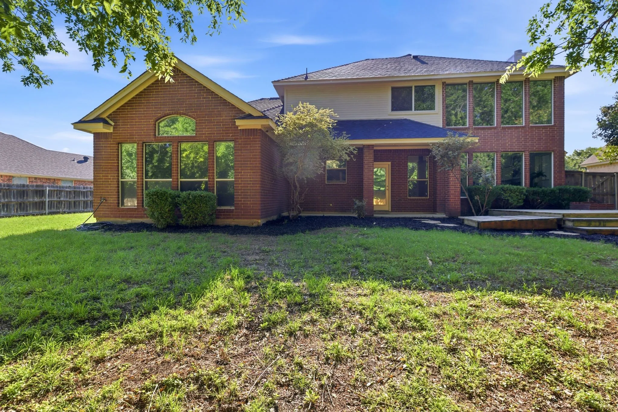 Two-story brick exterior featuring a covered patio, multiple large windows, and a multi-level wooden deck