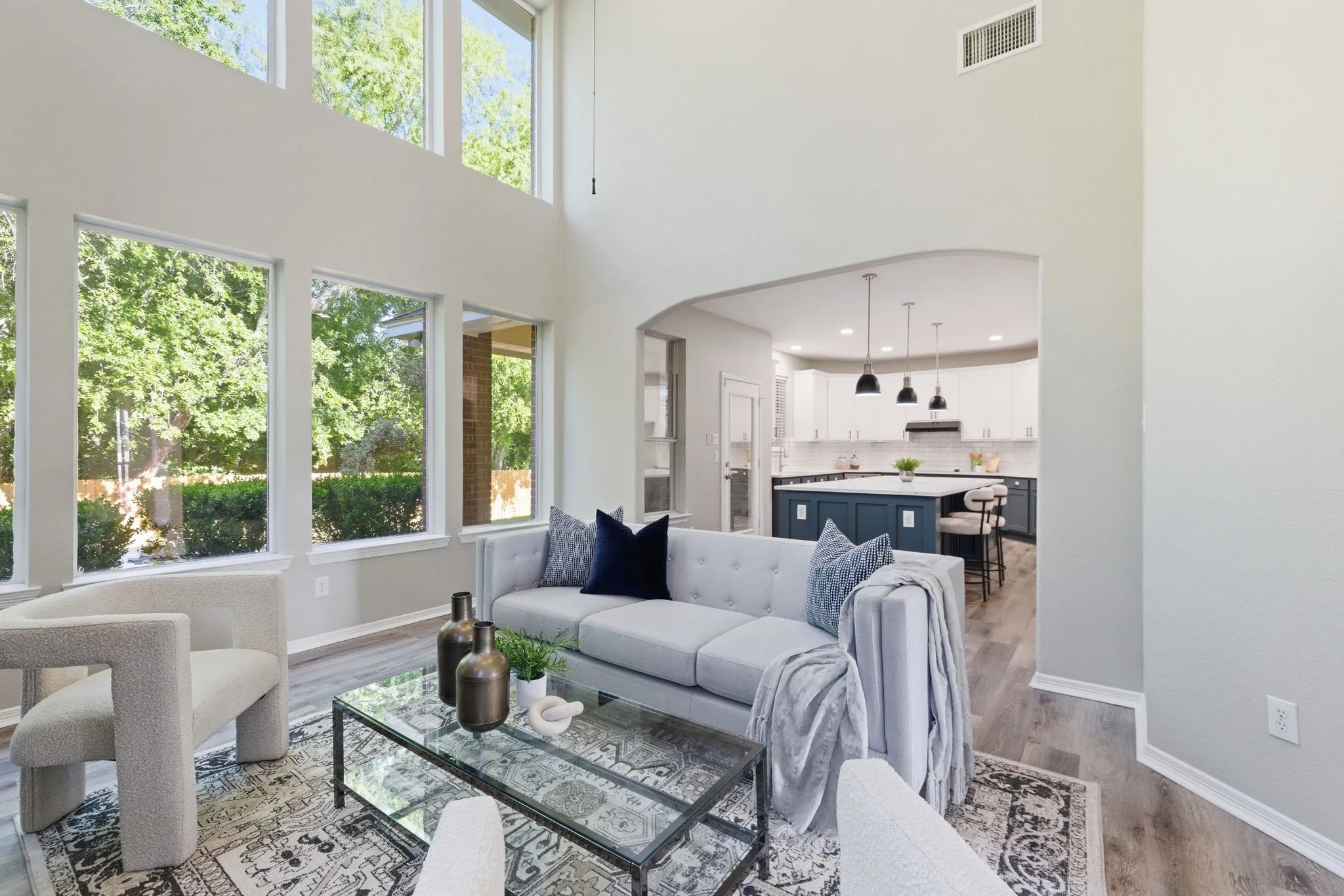 Two-story living area with high ceilings, multiple tall windows, wood-finish flooring, and an arched entryway to the kitchen